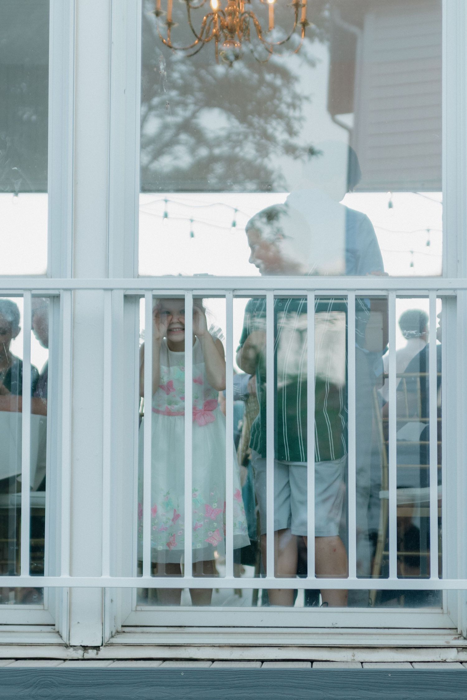 Group enjoying a relaxed moment on a white porch balcony with a chandelier visible overhead.
