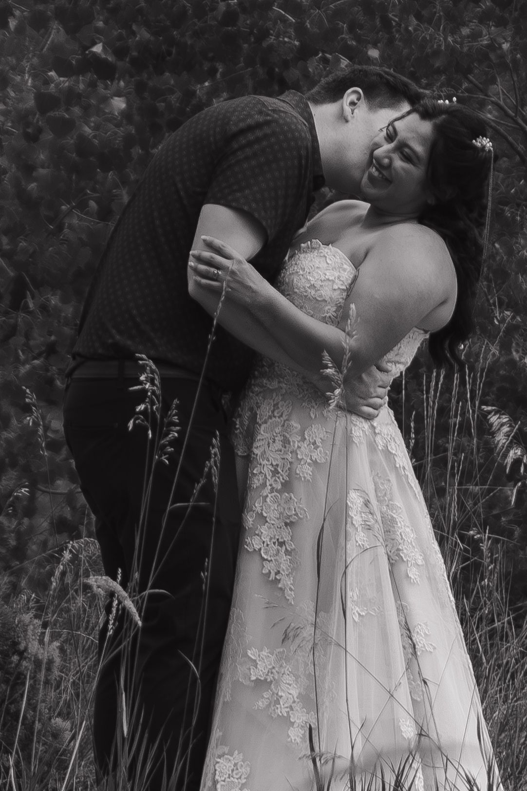 A romantic black and white photo series showing a couple embracing in tall grass with a white lace dress.