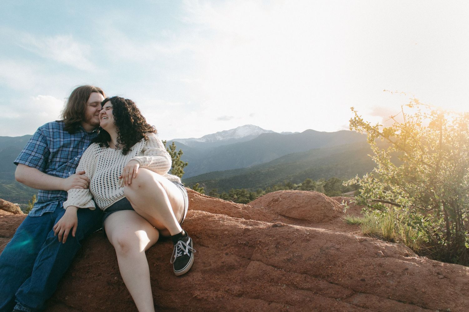 A romantic sunset photoshoot in the mountains with a couple embracing on red rocks.