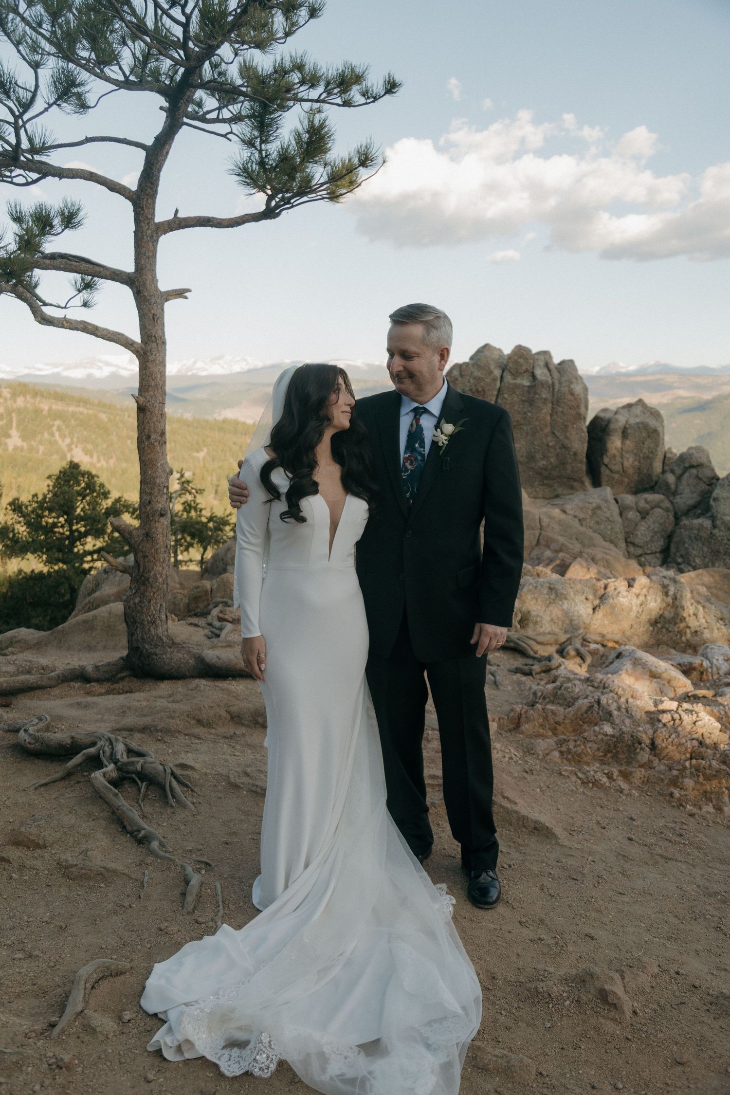 A bride and groom share a smile on a rocky mountain overlook with scenic views.