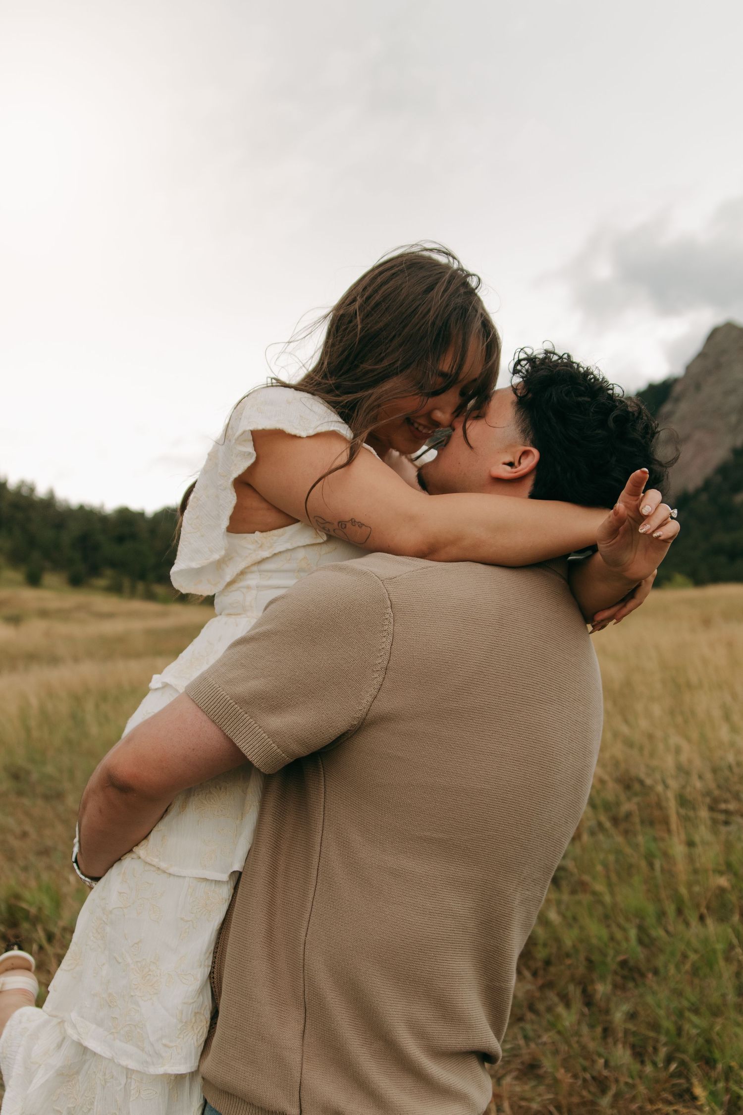 Couple sharing a romantic embrace in a golden field with mountains in the background.