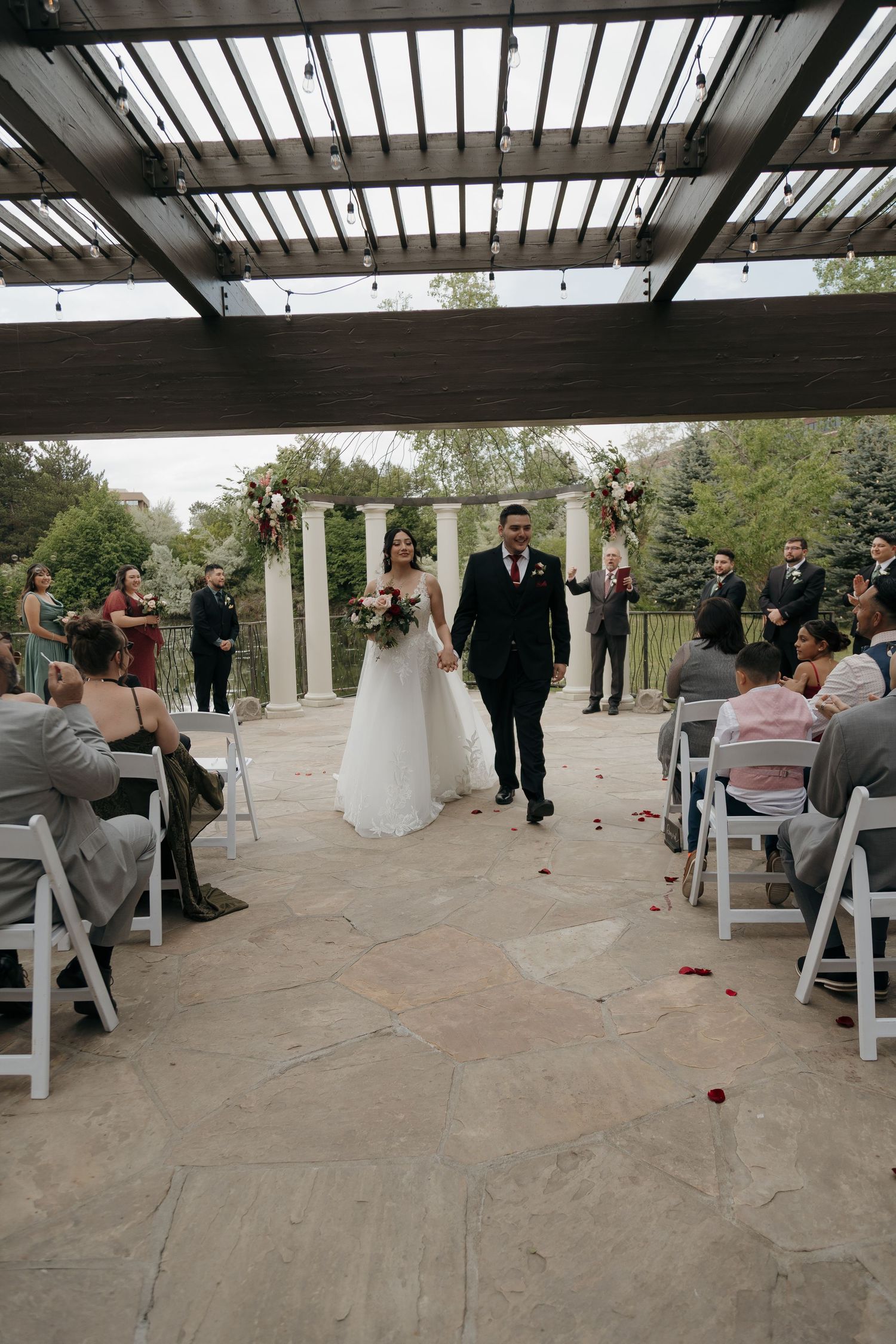 Newlyweds walk down the aisle together after wedding ceremony as guests celebrate with rose petals.