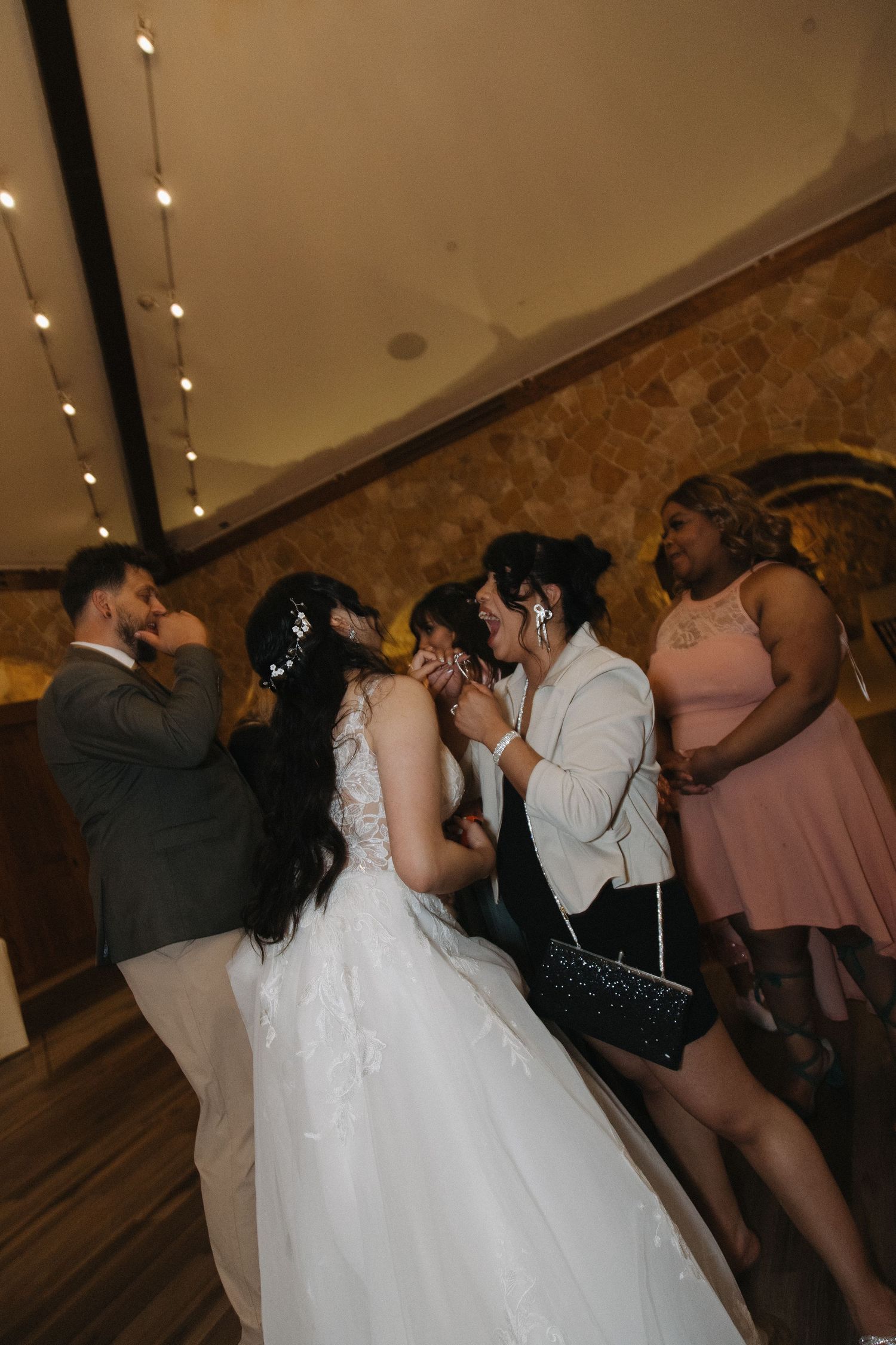 Bride in white gown socializing with guests at a warmly lit wedding reception.