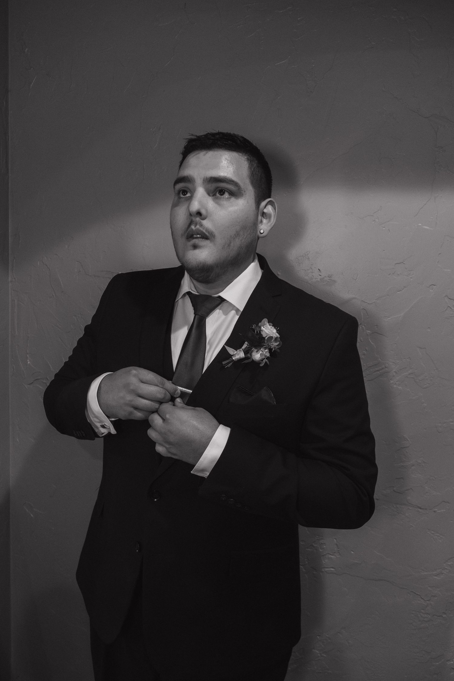 Black and white photo of a groom in a dark suit adjusting his cufflinks with a boutonniere on his lapel.
