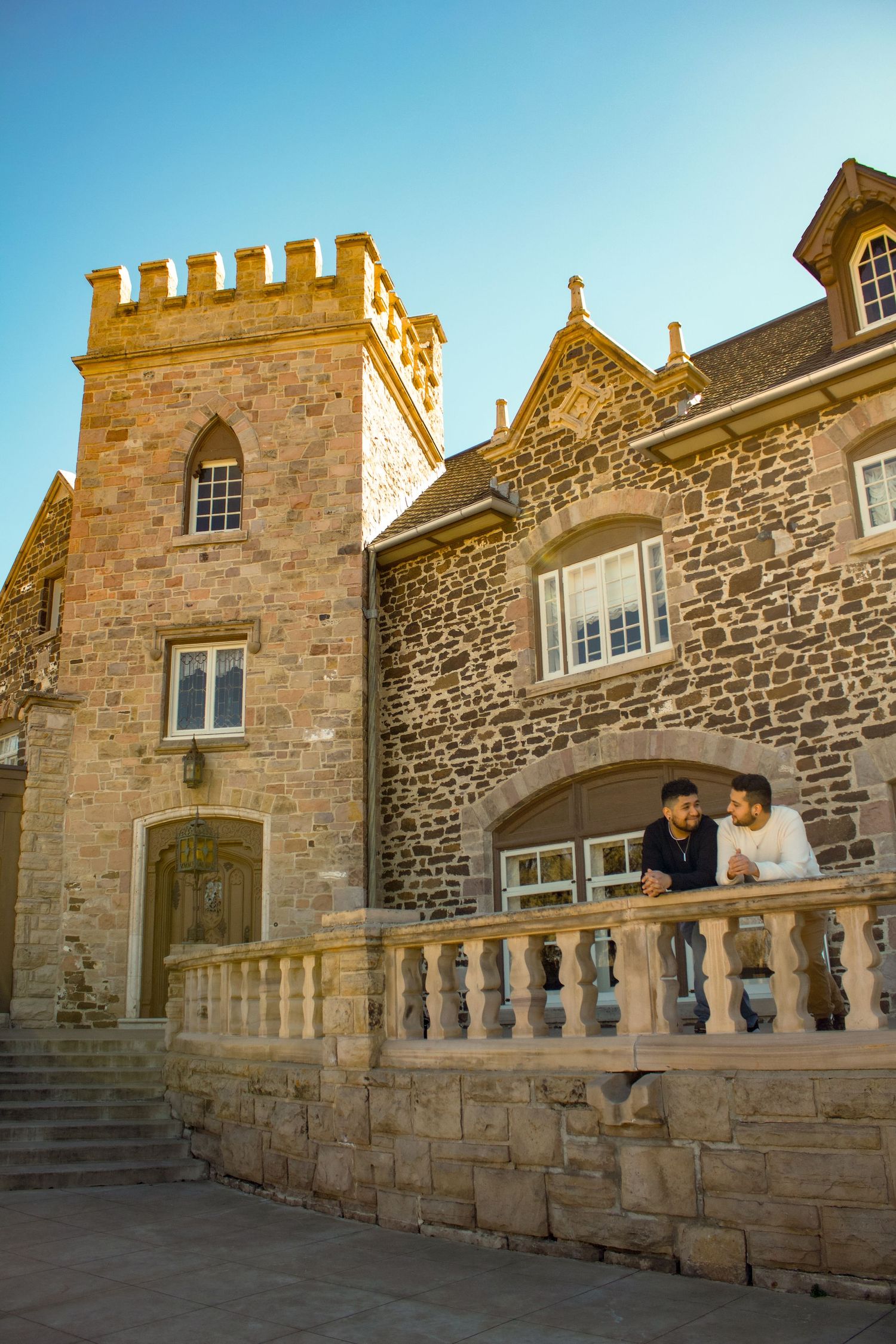 Couple standing on ornate stone balcony of historic castle-like building.