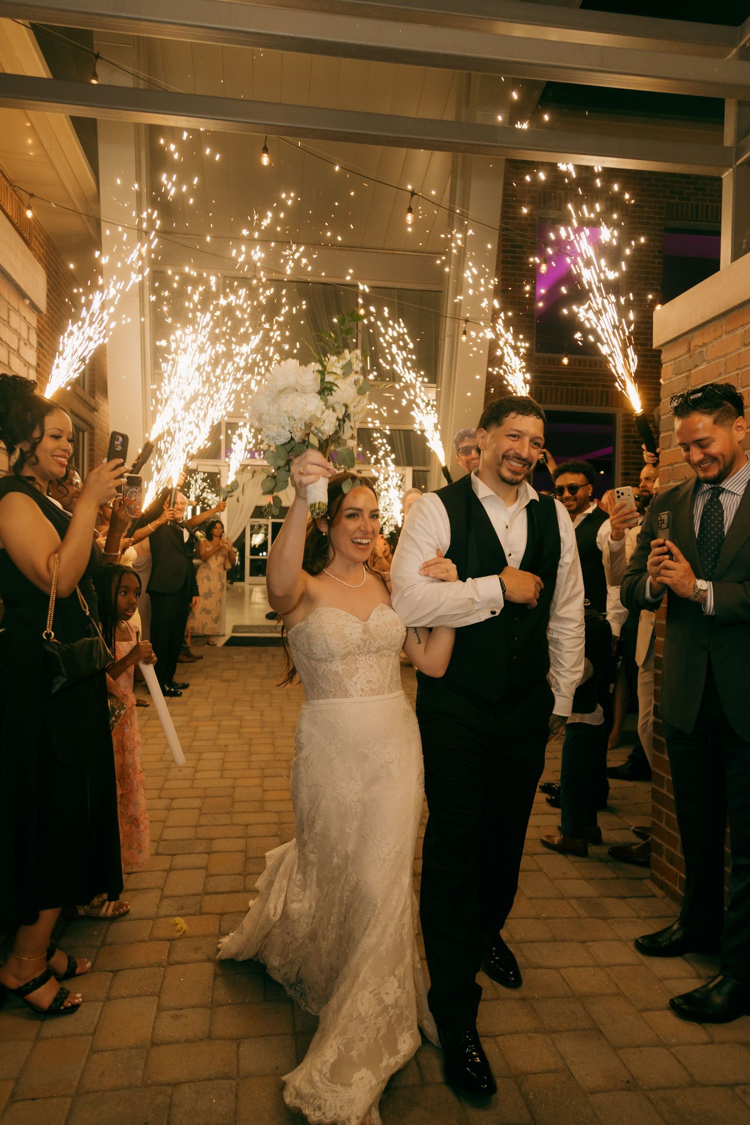 Bride and groom walk through sparkling cold sparkler exit surrounded by cheering wedding guests.