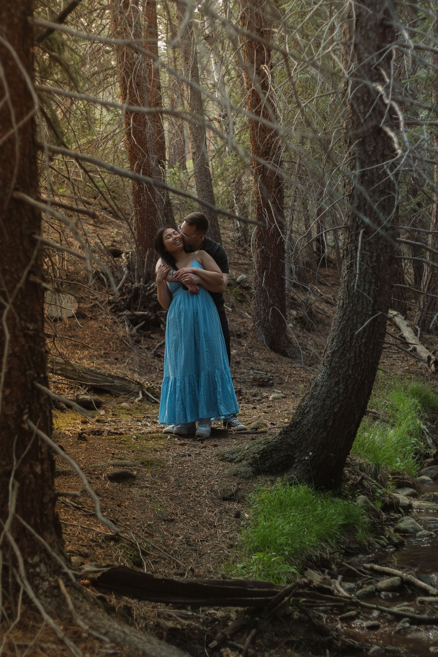 A romantic embrace captured on a serene forest path with natural lighting.