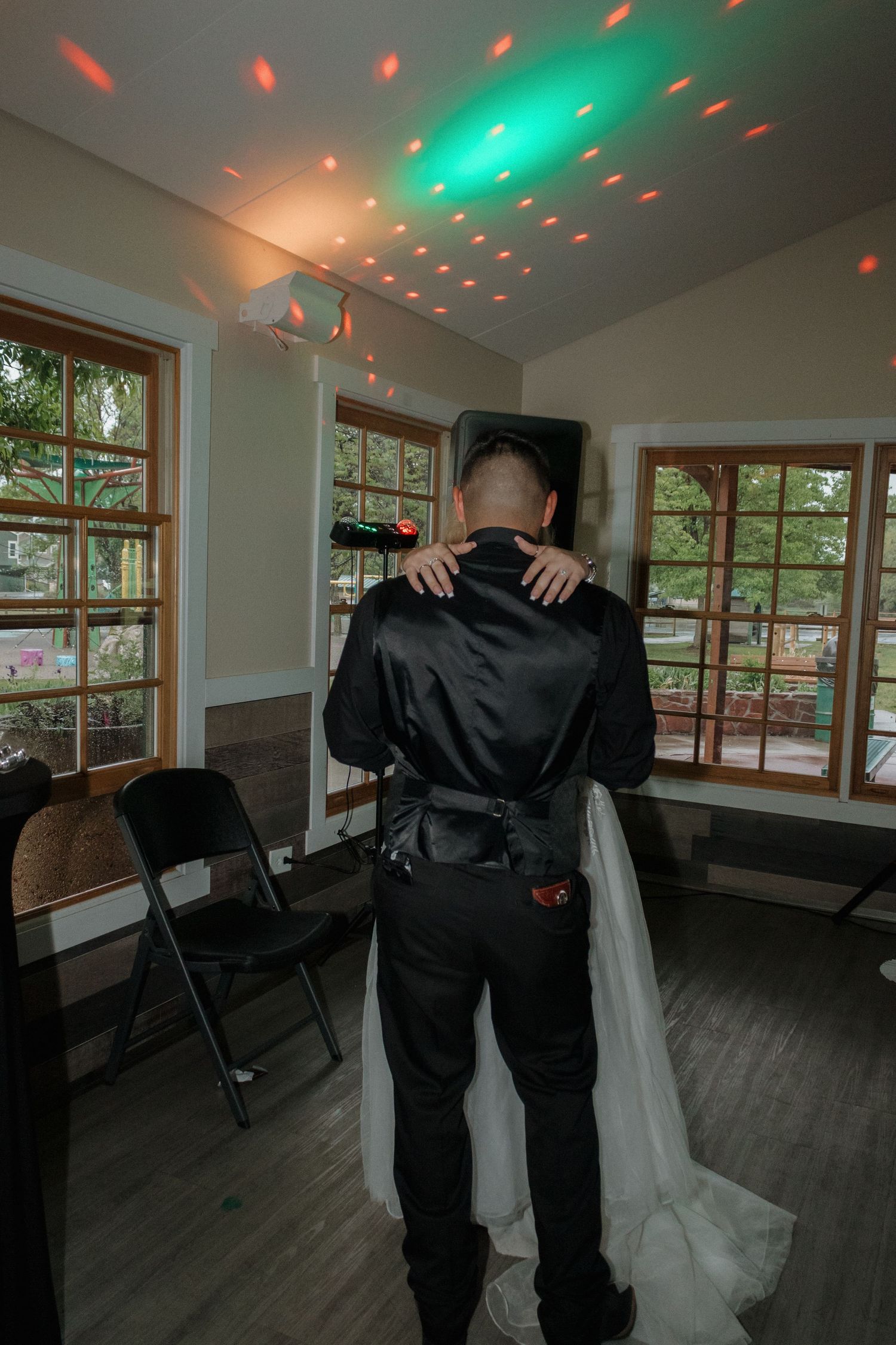 Red and green disco lights shine on the ceiling as a couple dances in a reception venue.