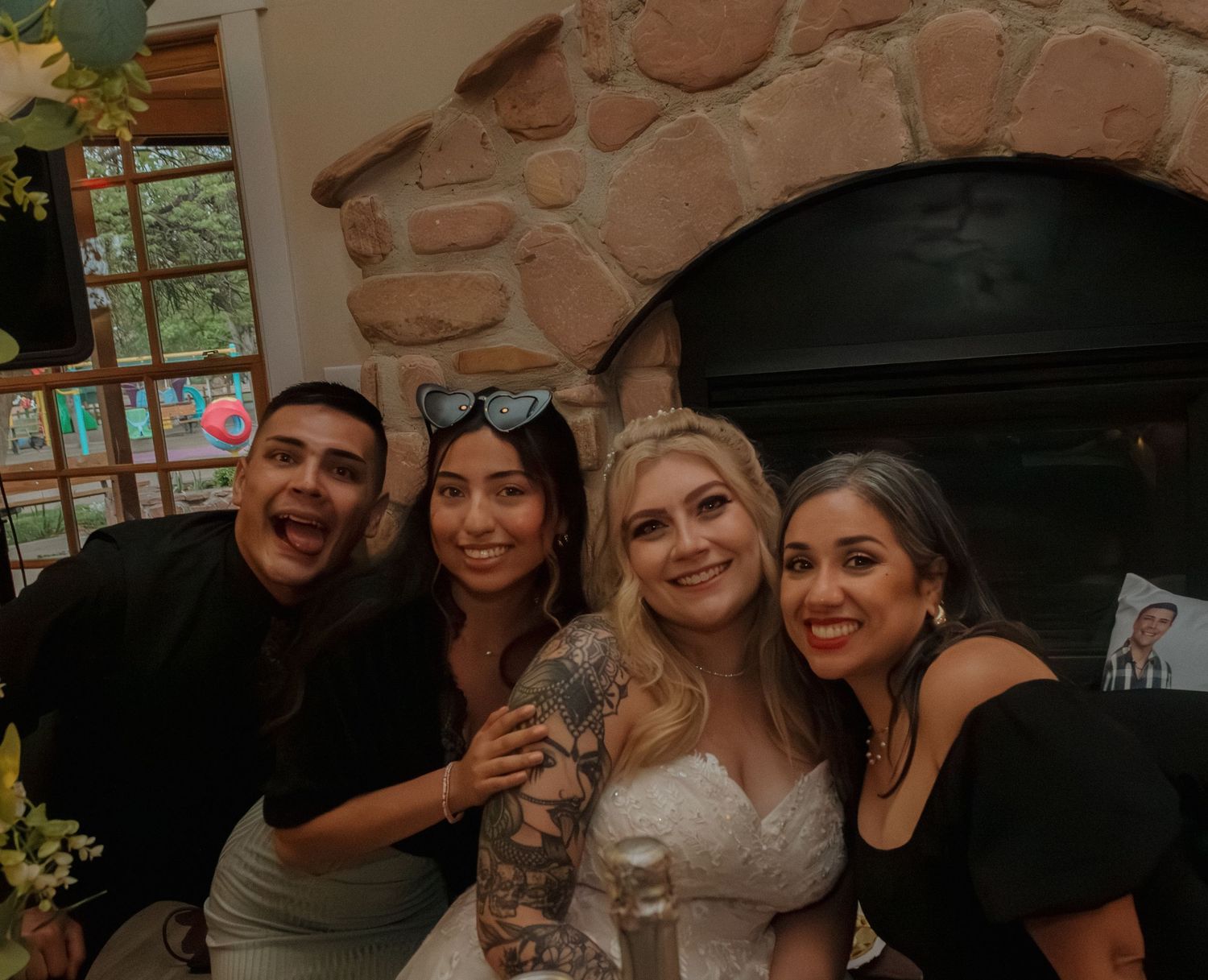 Wedding celebration group pose together near stone fireplace at reception venue.