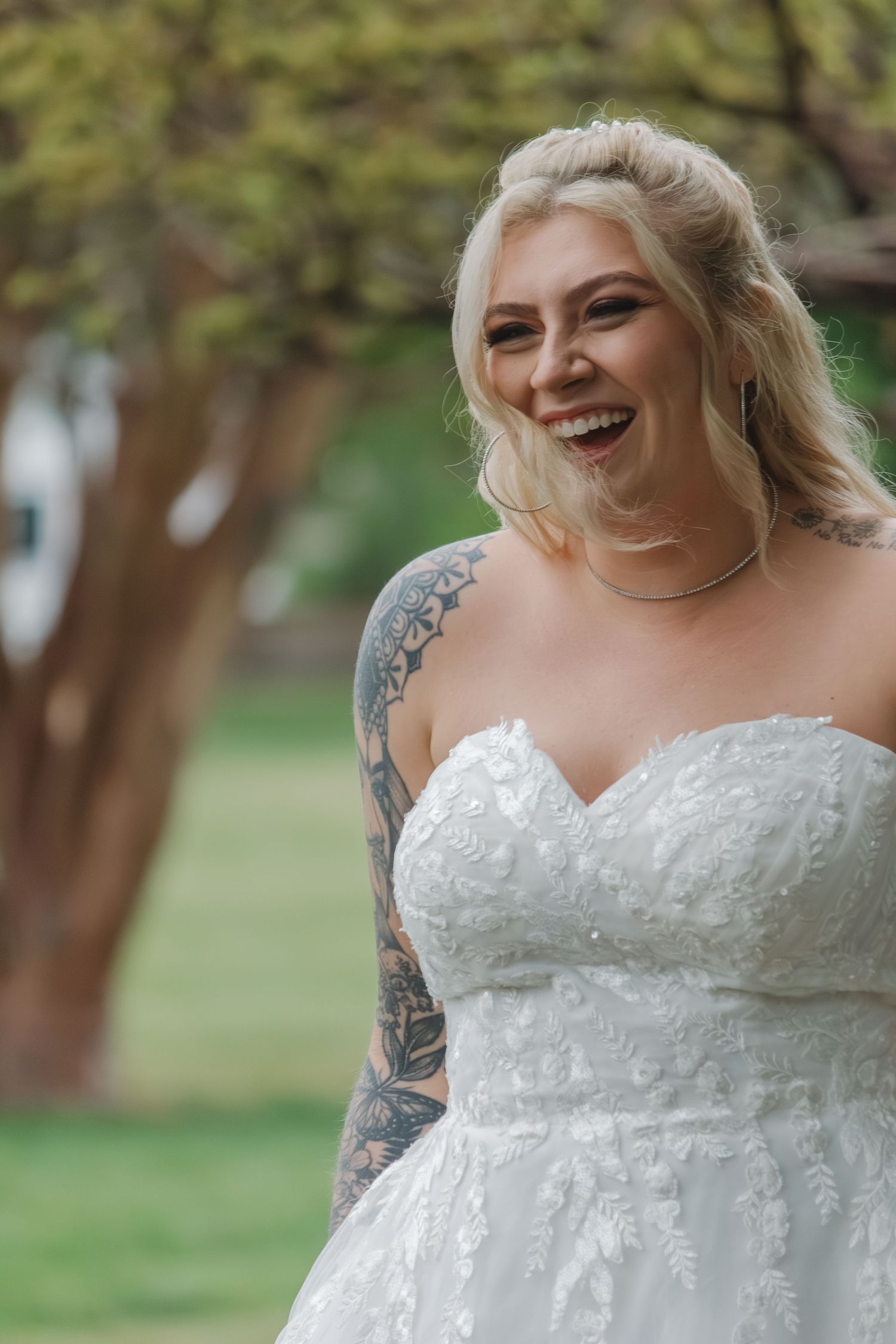 Bride in detailed lace wedding gown smiles radiantly outdoors.