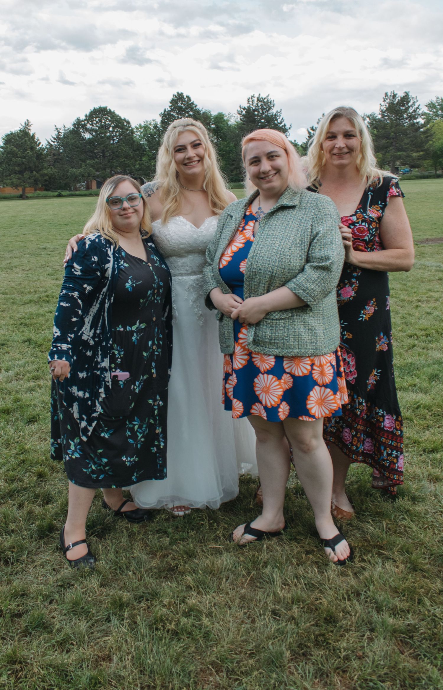 Small group poses for wedding photo outdoors with bride in white dress against green landscape.