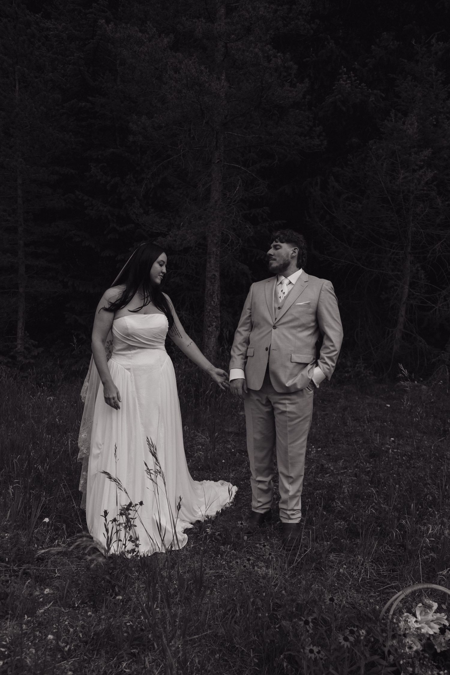 Black and white photo of bride and groom holding hands in a forest meadow during their elopement.