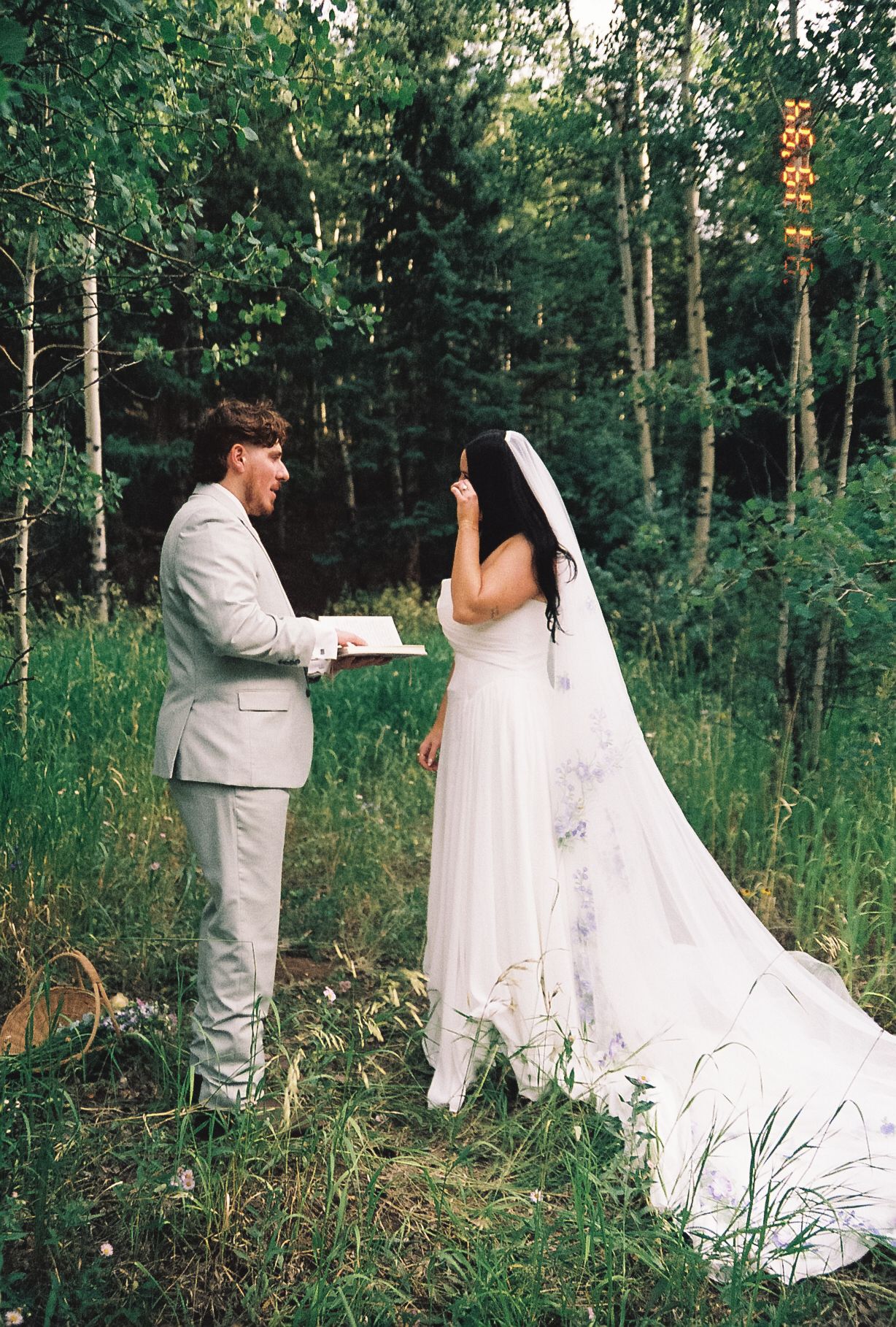 Groom reads vows to emotional bride during intimate forest elopement ceremony among aspen trees.