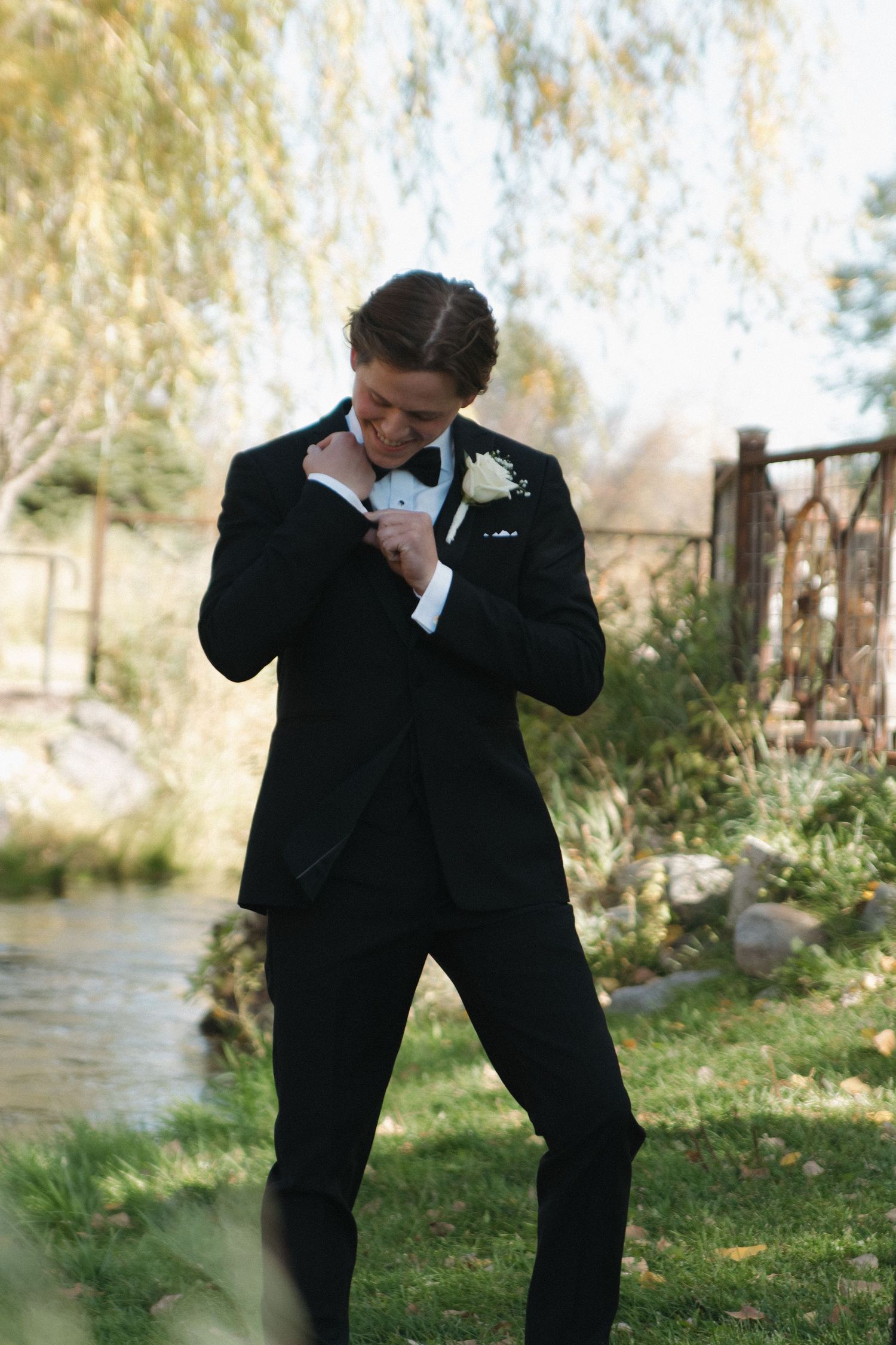 Playful groomsmen in black tuxedos dancing and celebrating outdoors.