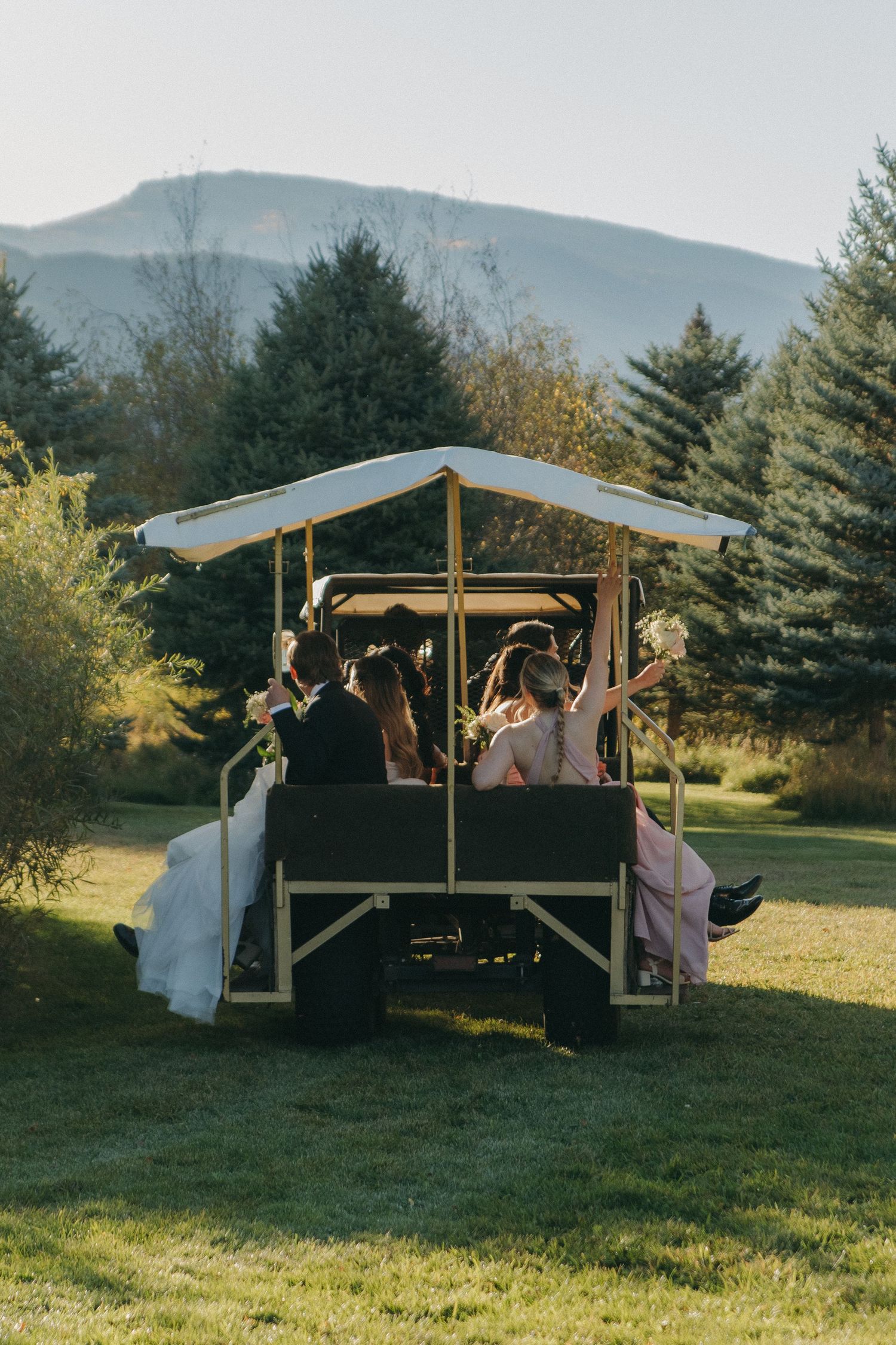 A group enjoying a covered outdoor gathering space in a grassy field with mountains in the background.