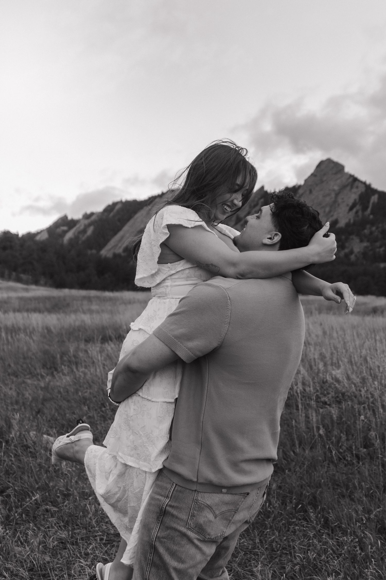 Couple embracing in a field with rocky mountain flatirons in the background, black and white photo.