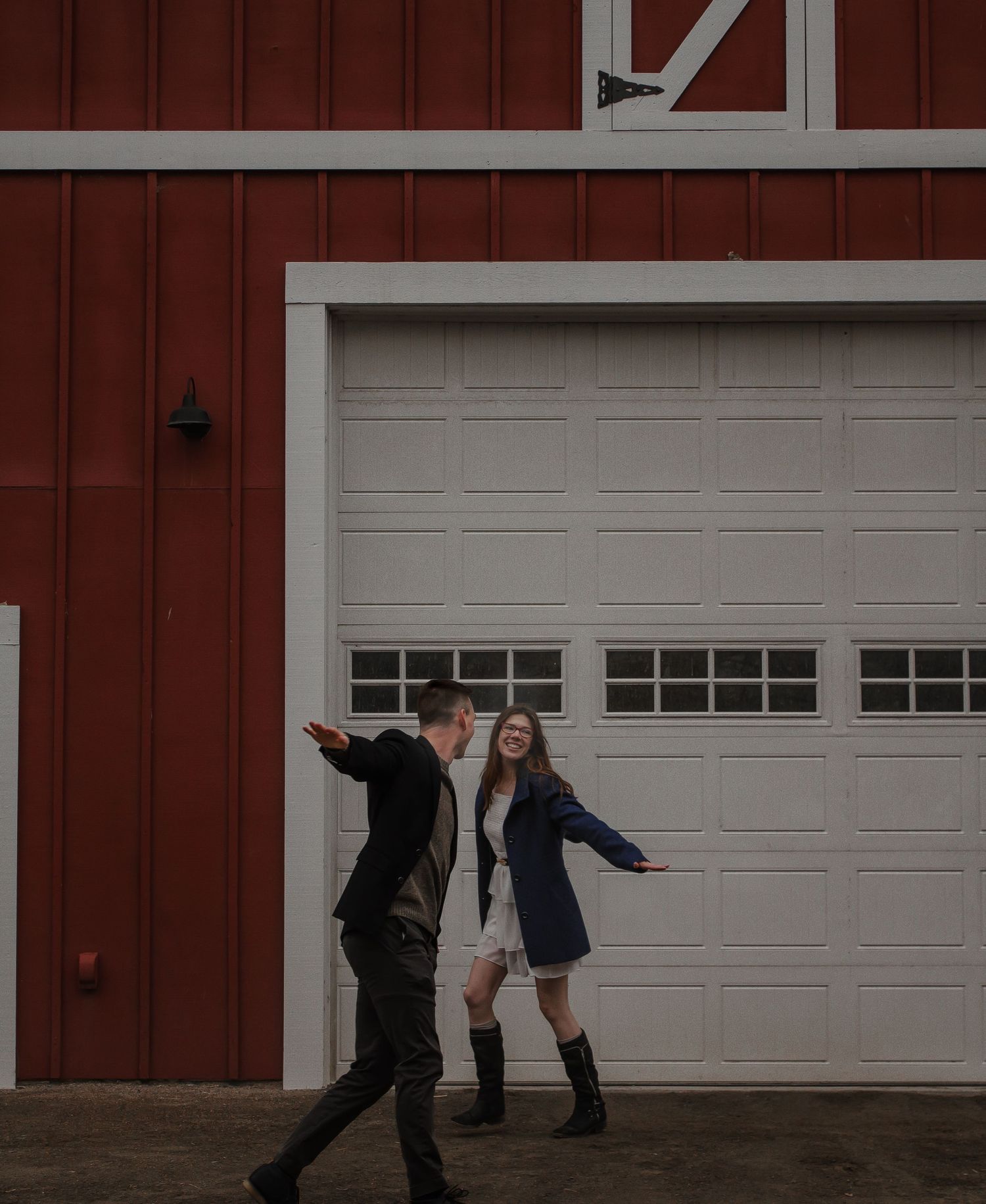 A couple dancing playfully in front of a red barn with a white garage door.