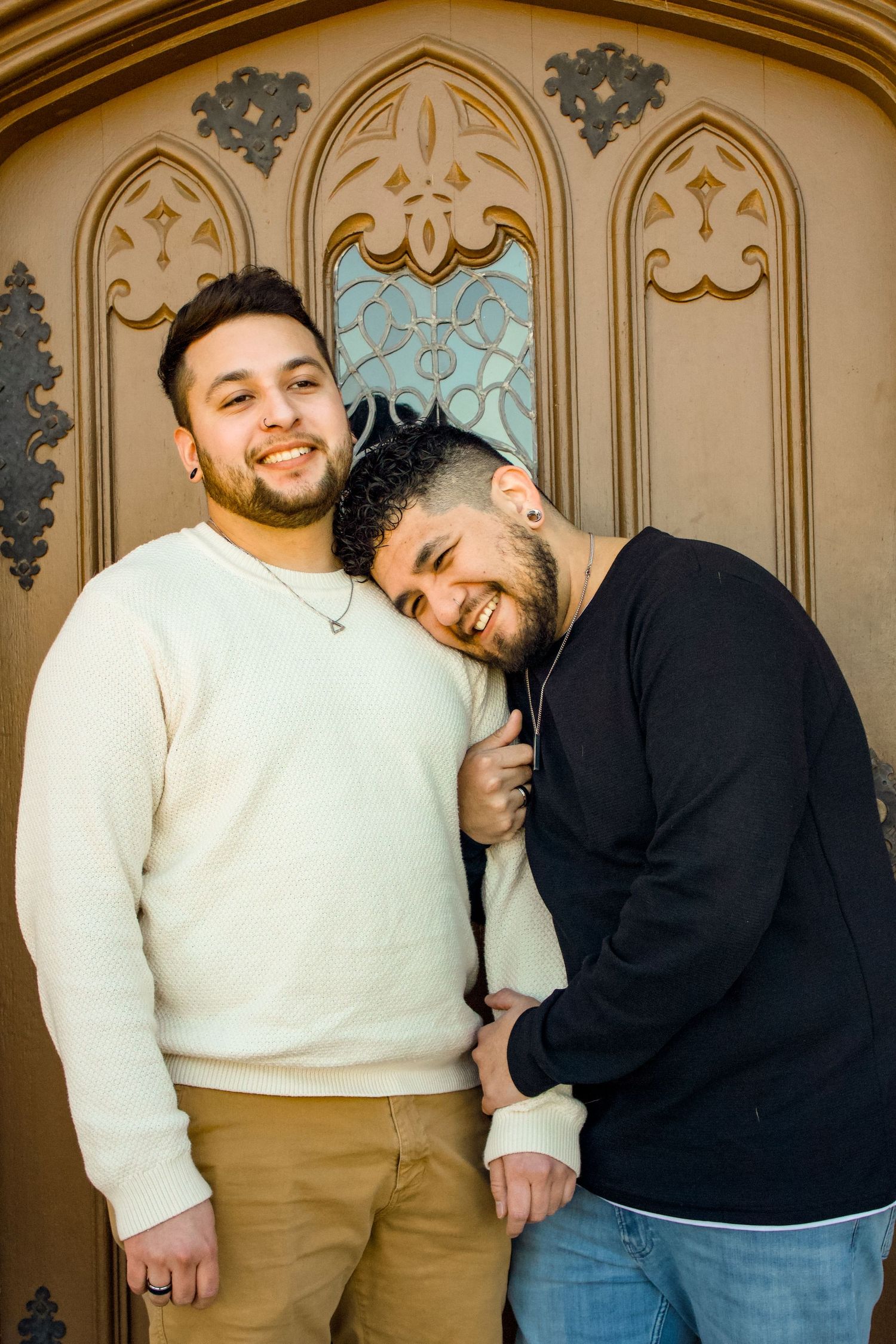 Two people in casual attire sharing a joyful moment against an ornate architectural background.