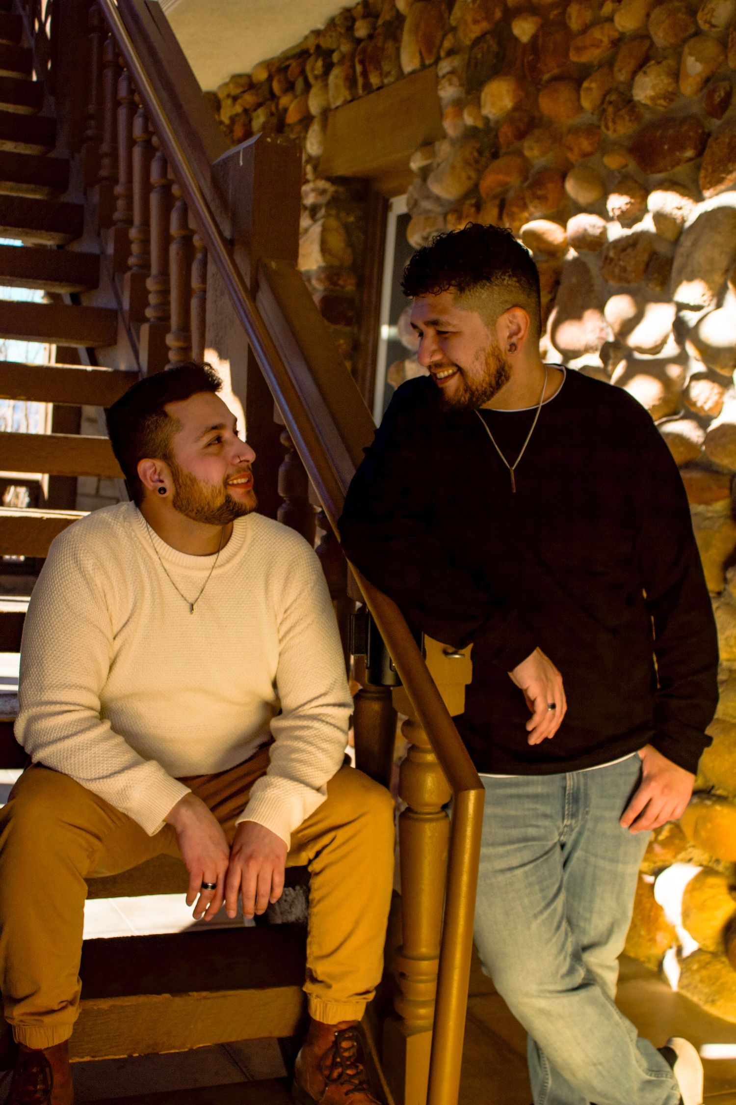 Two people share a warm conversation while sitting on wooden stairs with stone wall backdrop.