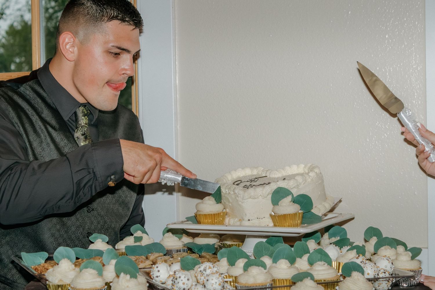 Wedding cake and dessert spread decorated with greenery on an elegant display table.