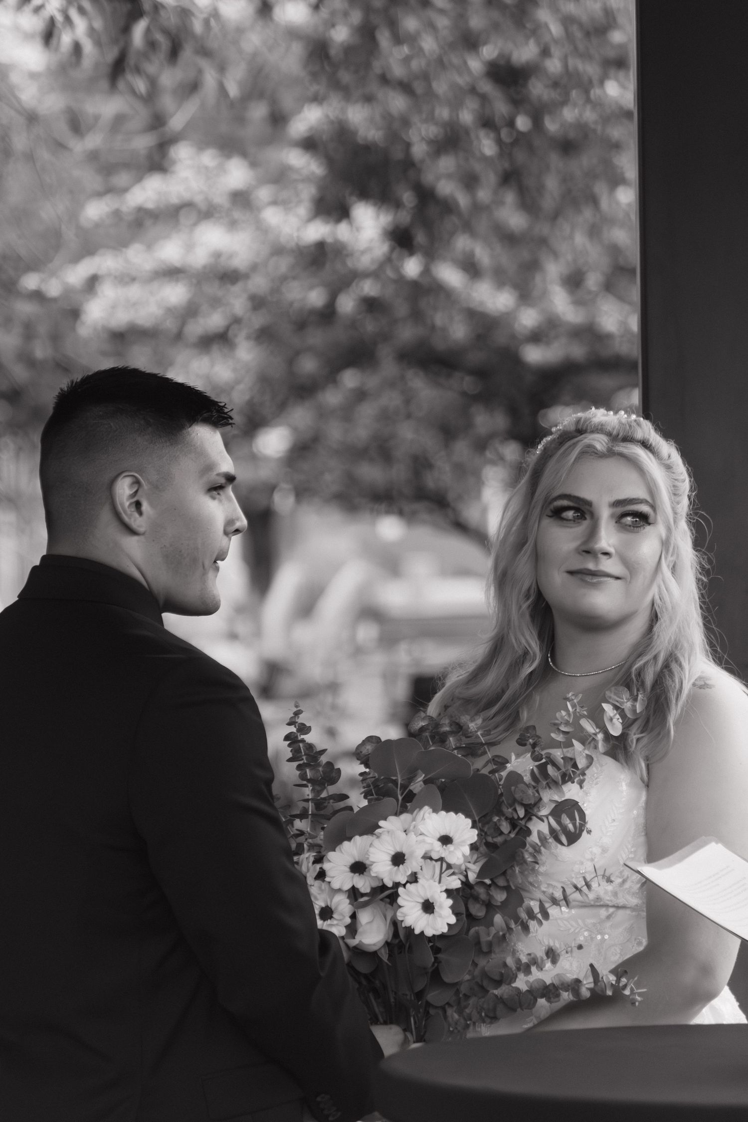 A black and white portrait of a couple at a wedding, with the bride holding a bouquet of white flowers.