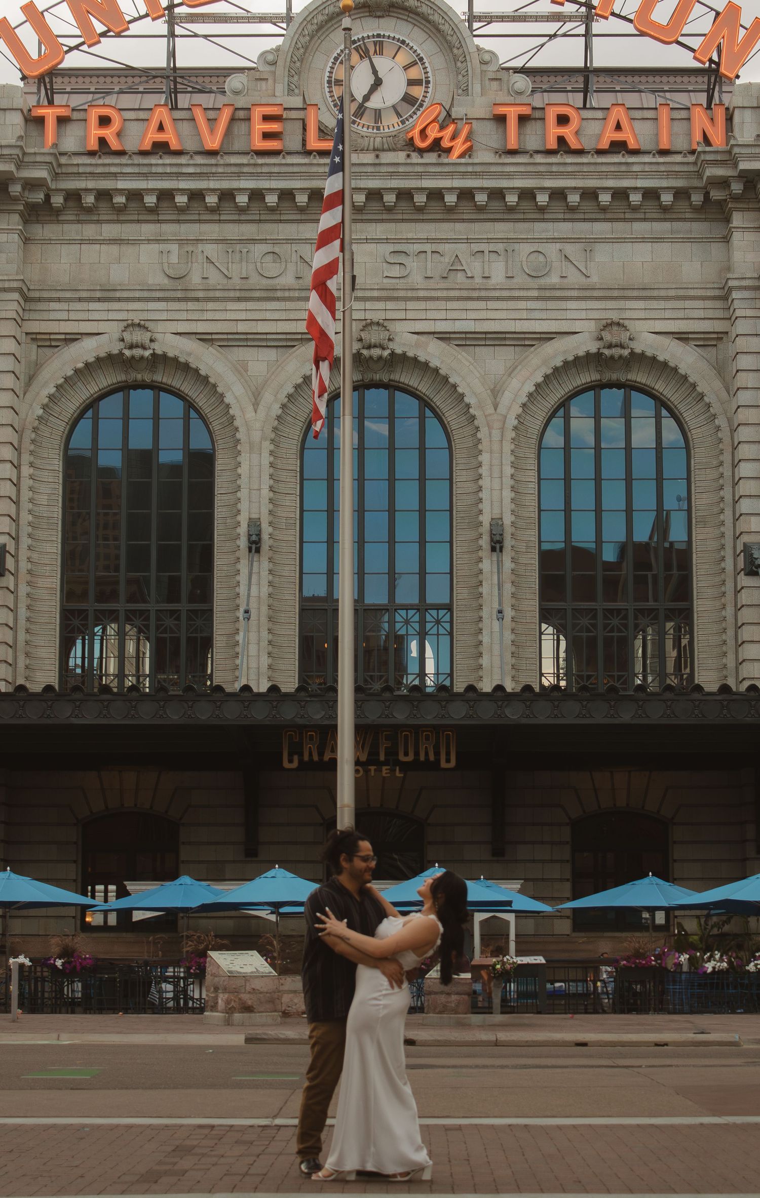 A couple dancing in front of the historic Union Station with 'Travel by Train' signage.