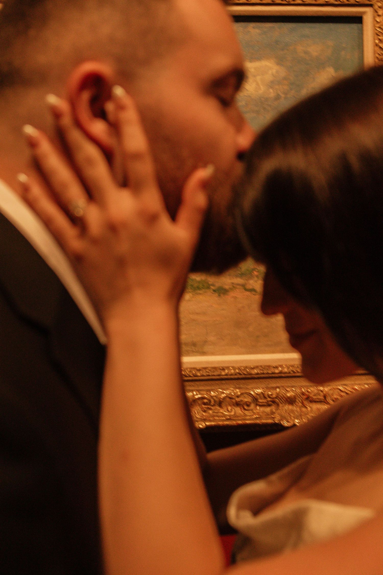 Close up of a tender romantic kiss with ornate gold frame artwork in background.
