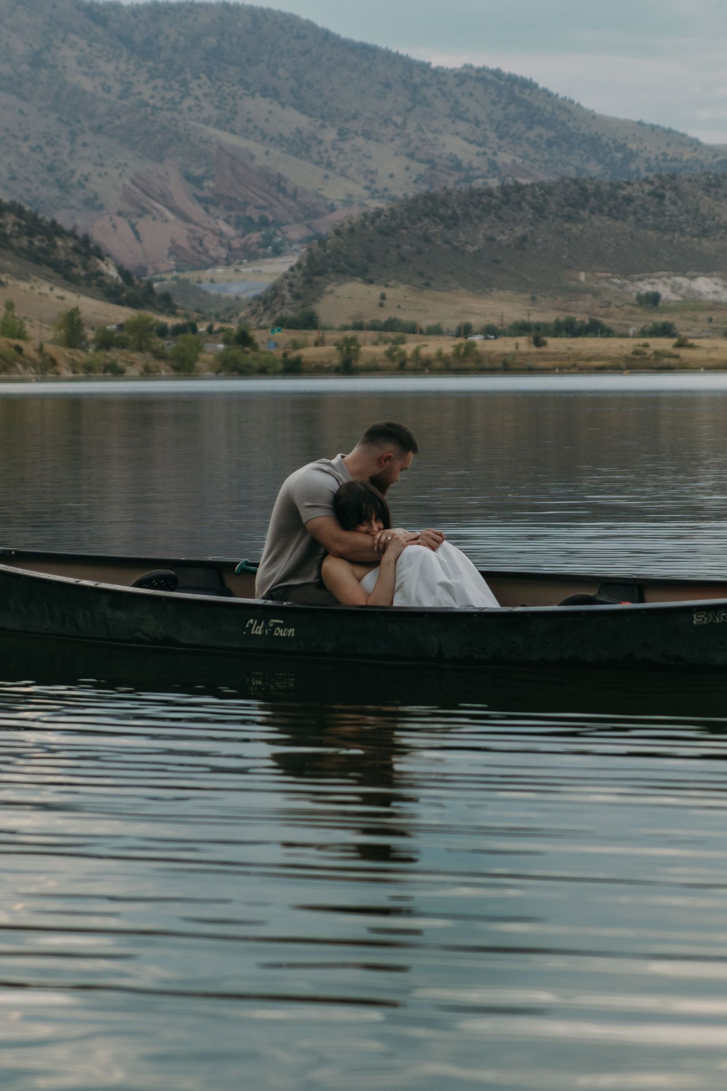A romantic couple shares an intimate moment while lounging in a canoe on a calm mountain lake.