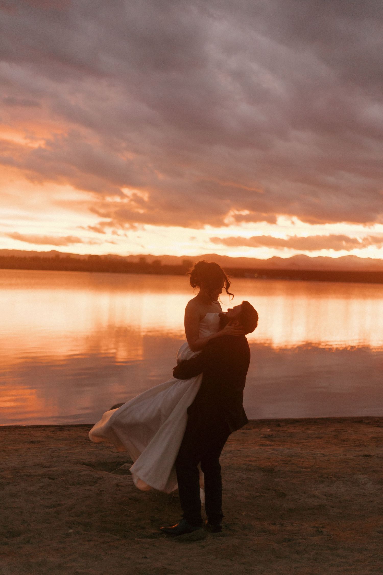 A romantic couple embracing on a beach at sunset with dramatic orange clouds.
