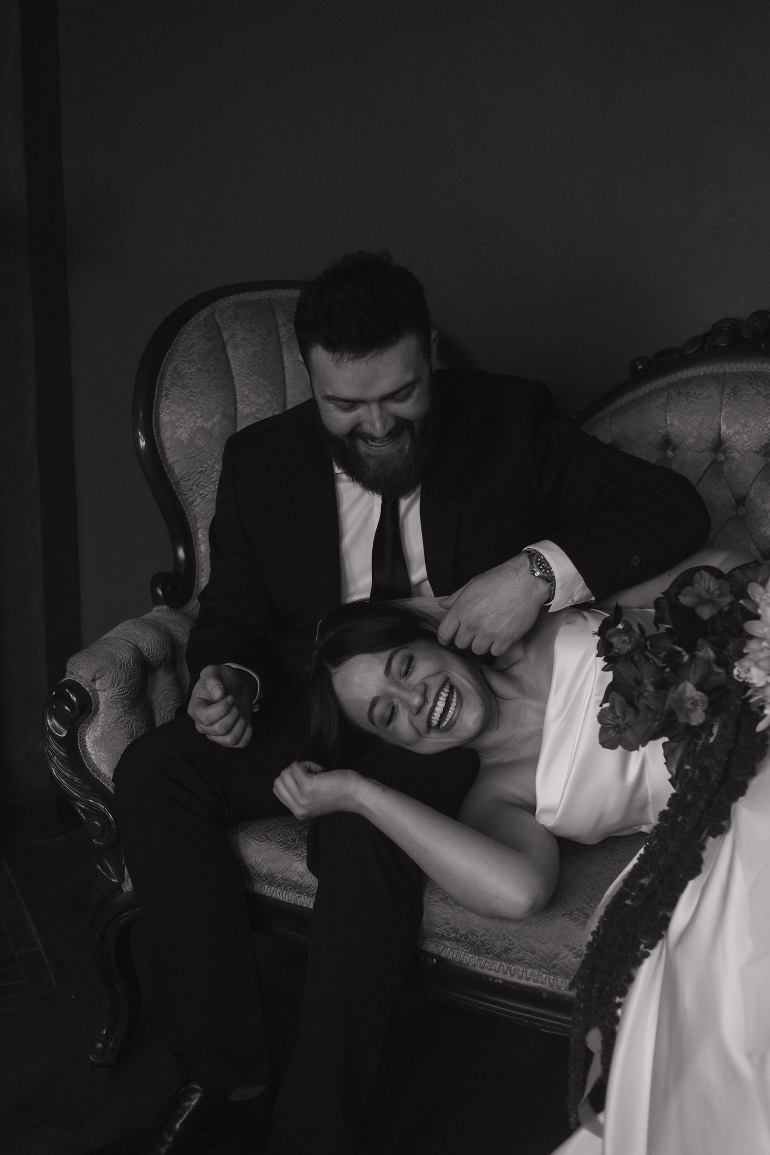 A romantic black and white portrait of a couple sharing an intimate moment on an antique chair.