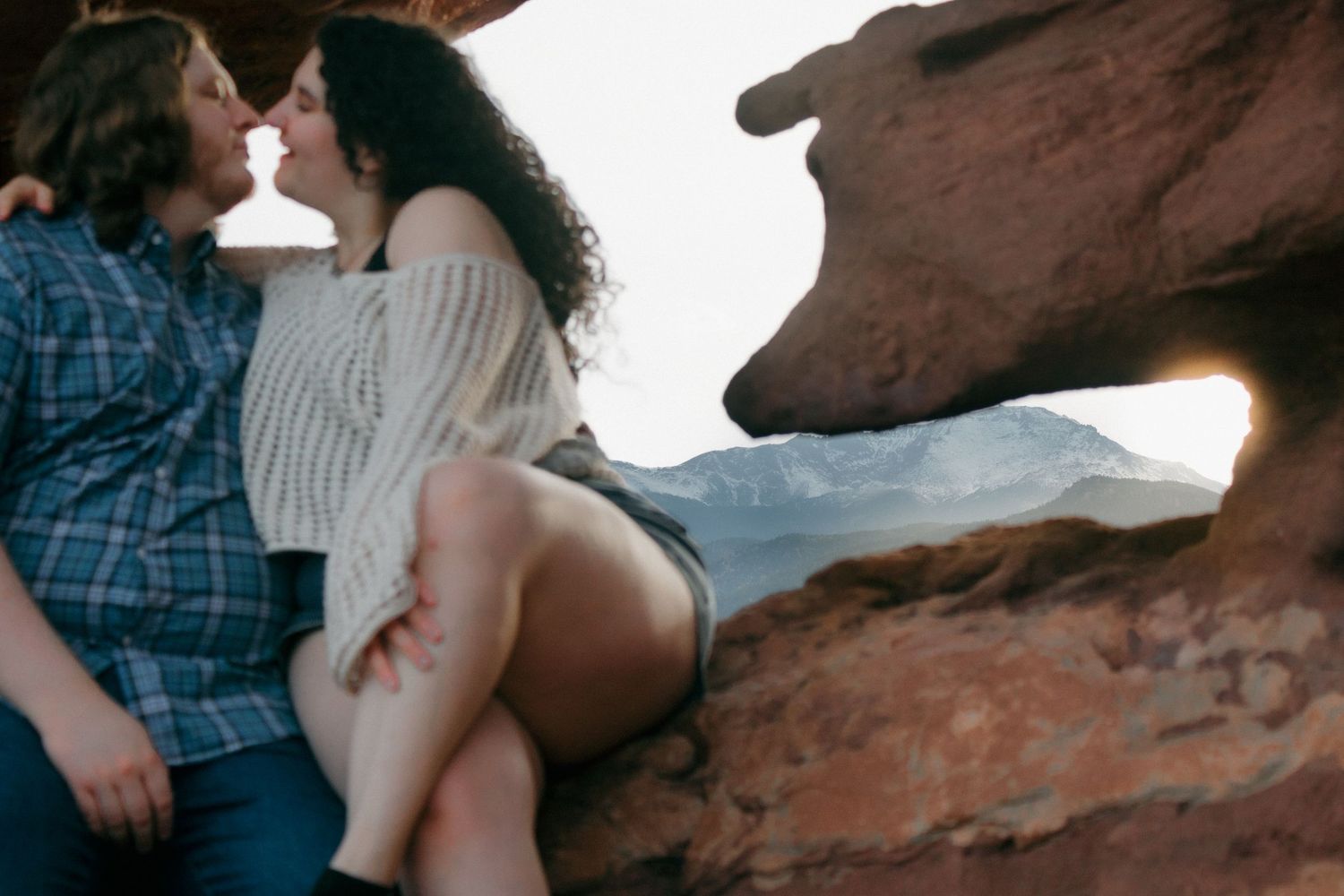 A couple sitting on red rocks at sunset with mountains in the background.