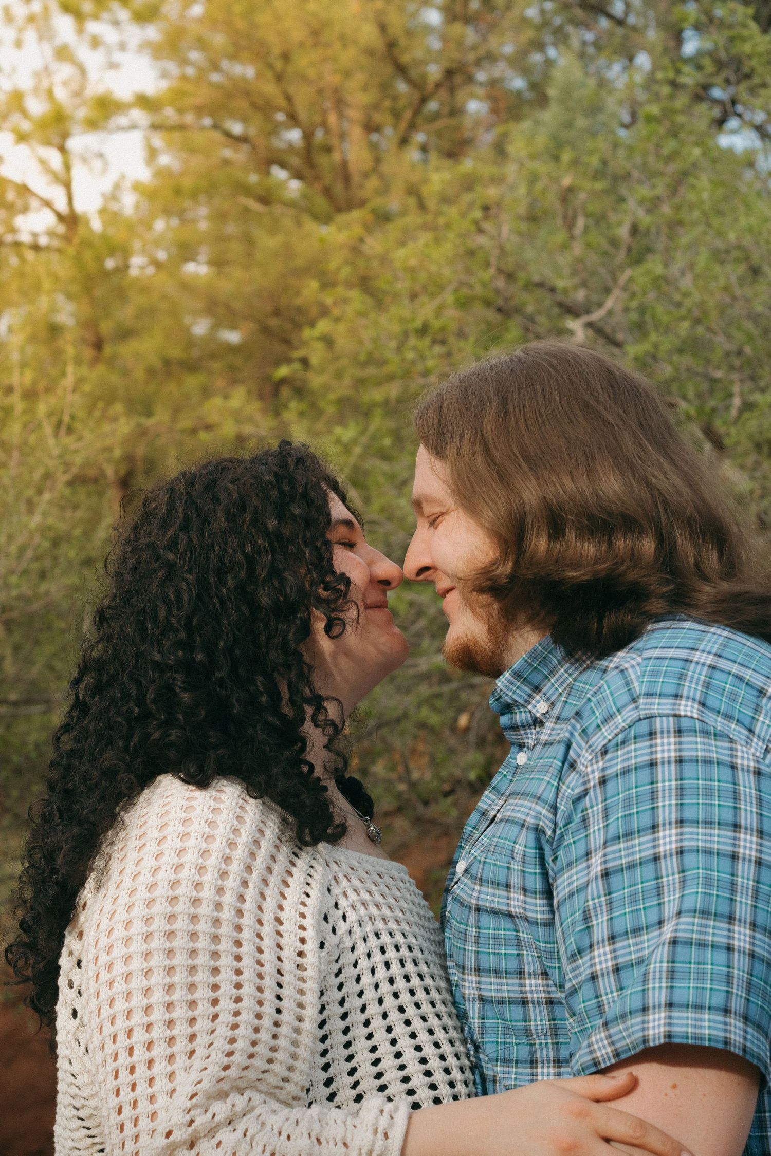 Couple sharing an intimate moment on a nature trail in warm sunlight.