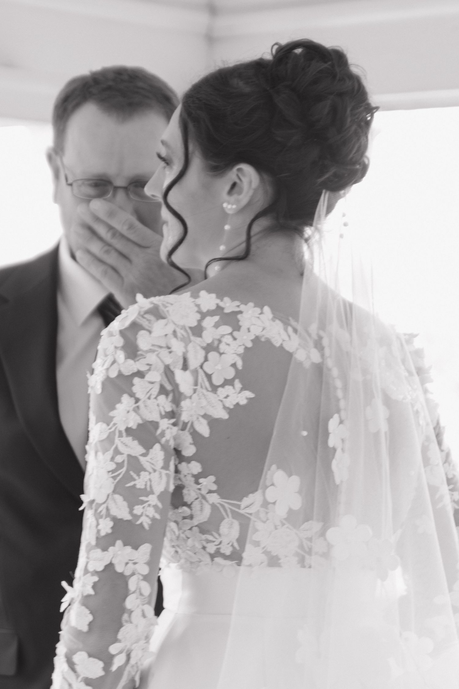A romantic wedding moment captured in soft black and white with delicate lace veil details.