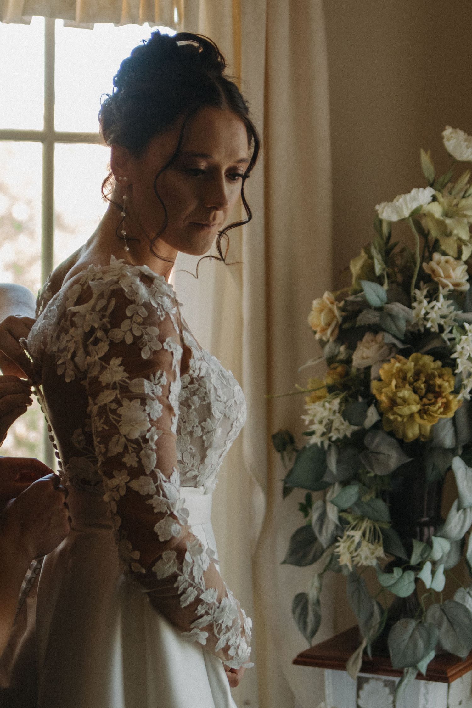 Elegant wedding dress with floral lace details photographed near a sunlit window.