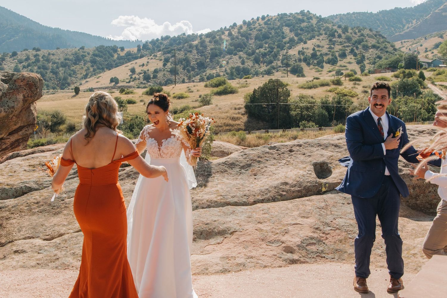 Wedding guests gather on a scenic mountain overlook during a bright sunny day.
