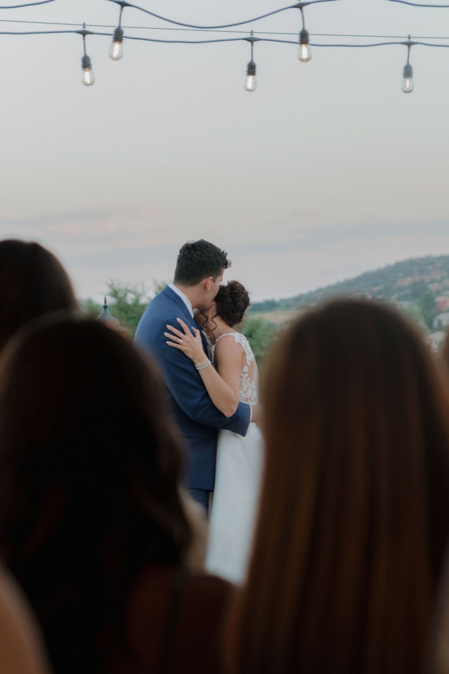 String lights frame a romantic outdoor wedding moment against a dusky sky.