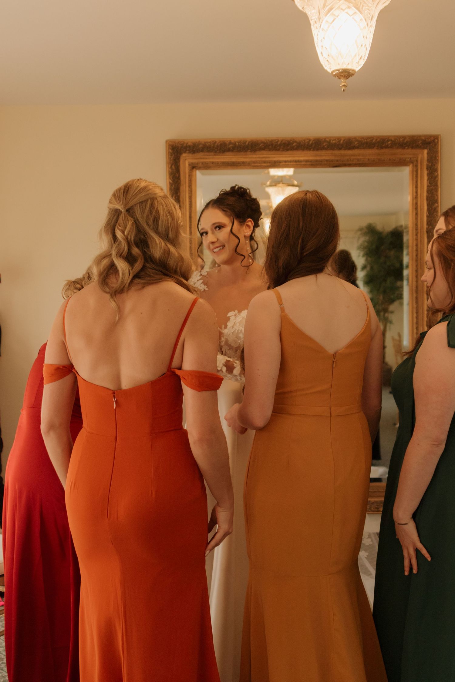 Wedding party members in coordinating warm-toned dresses stand together in an indoor venue.