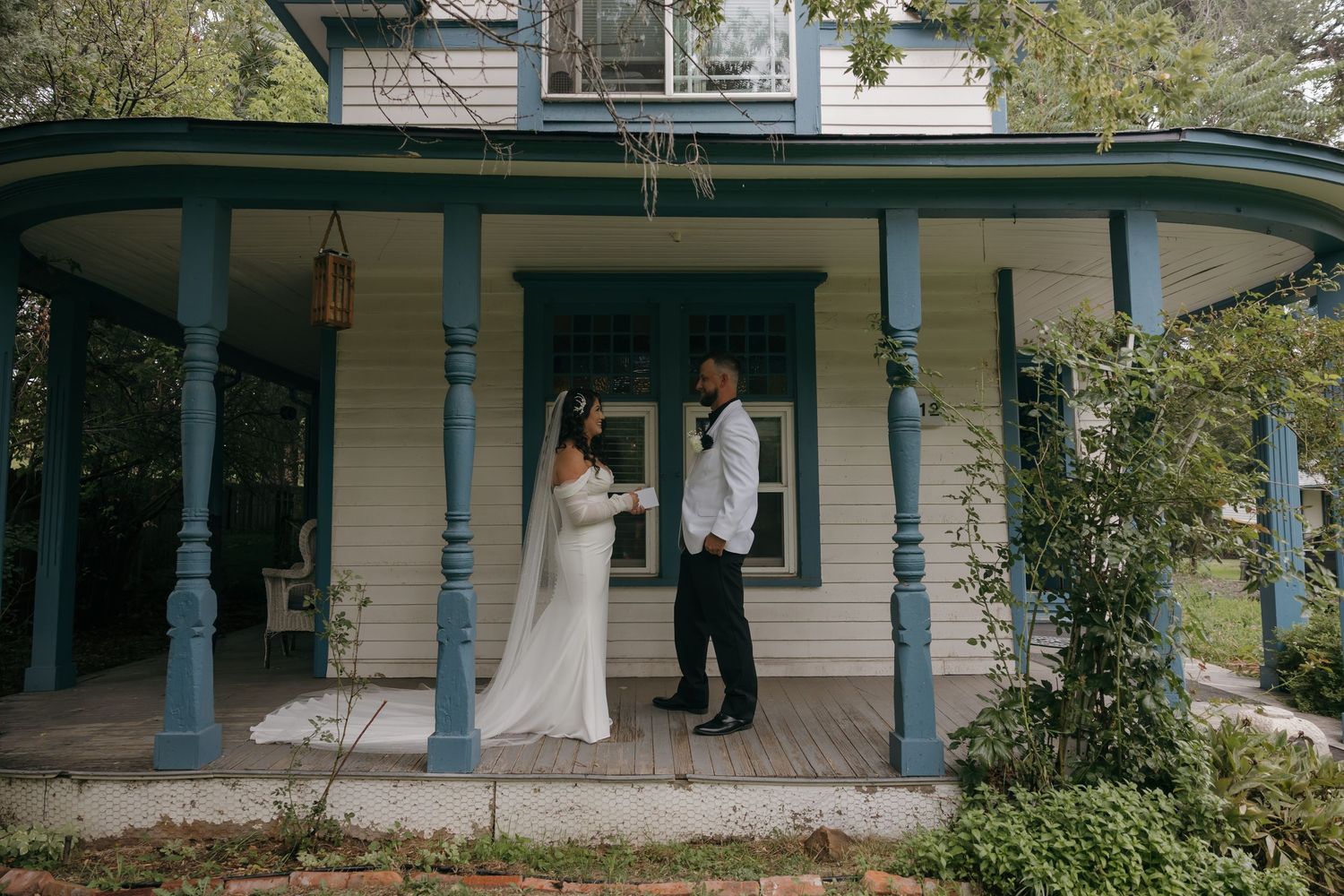 Bride and groom share a romantic first look on a charming blue and white Victorian porch.