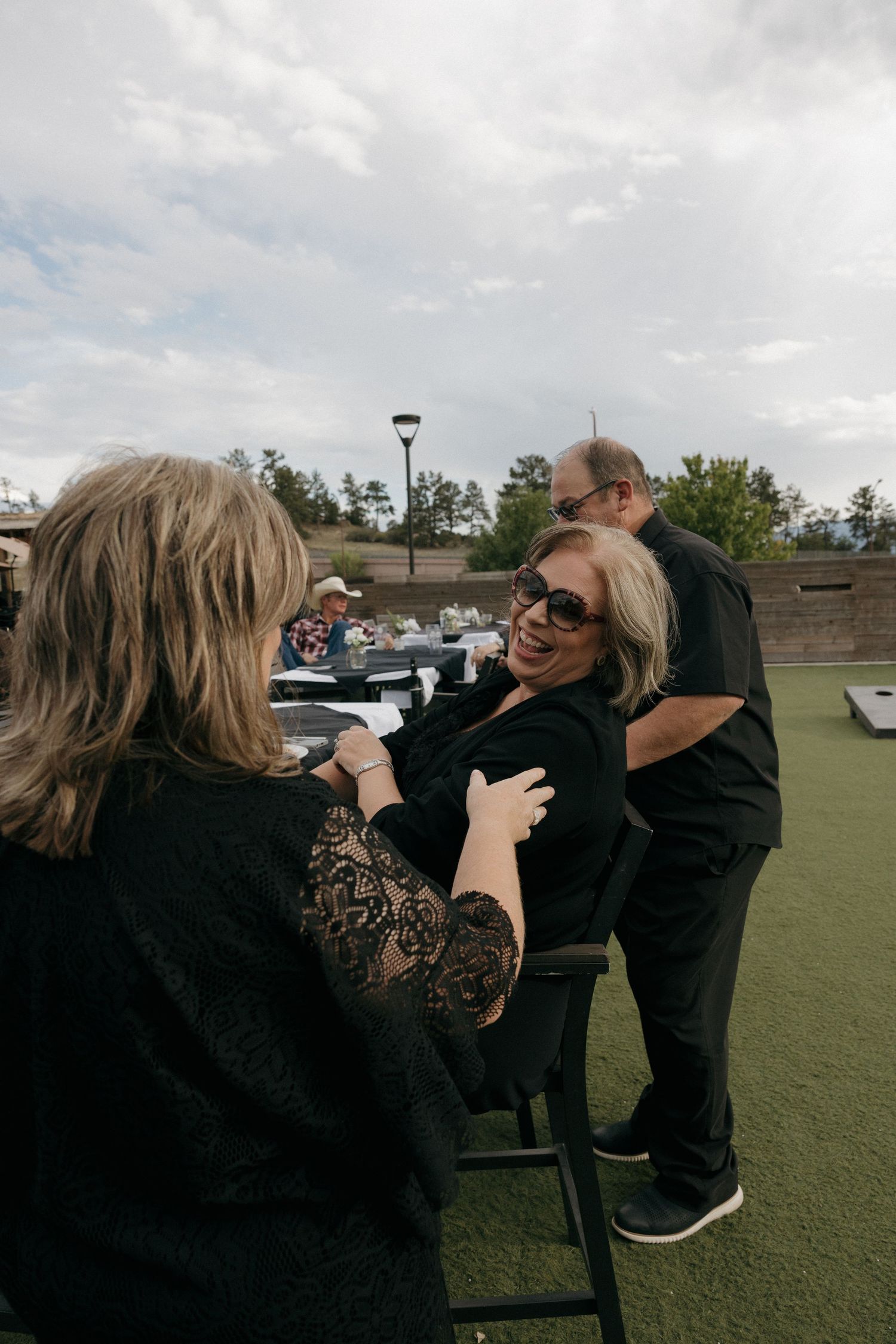 Wedding guests in black attire socialize outdoors on a patio during a wedding reception.