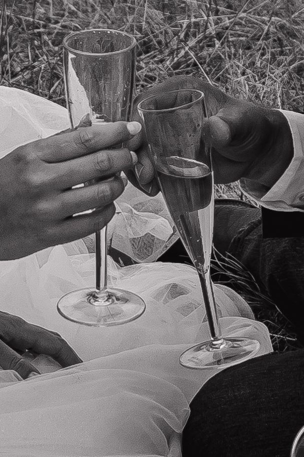 Black and white photo of champagne glasses clinking during a wedding toast.