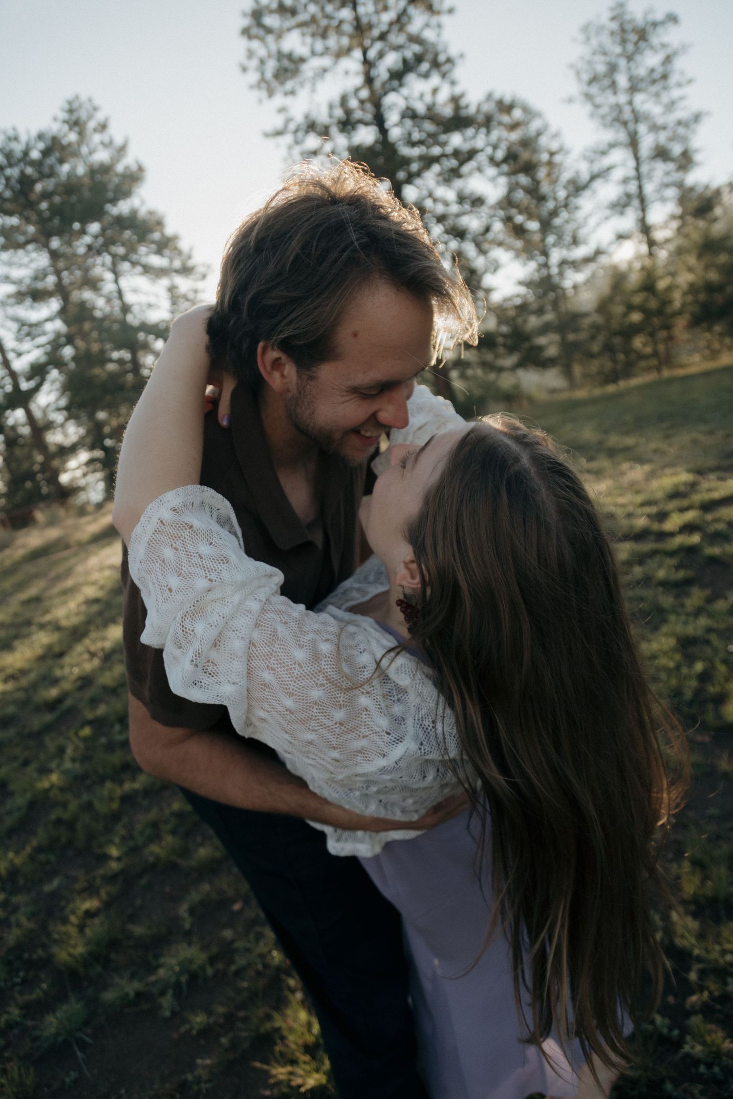 Romantic couple embracing and smiling in sunlit forest meadow during golden hour.