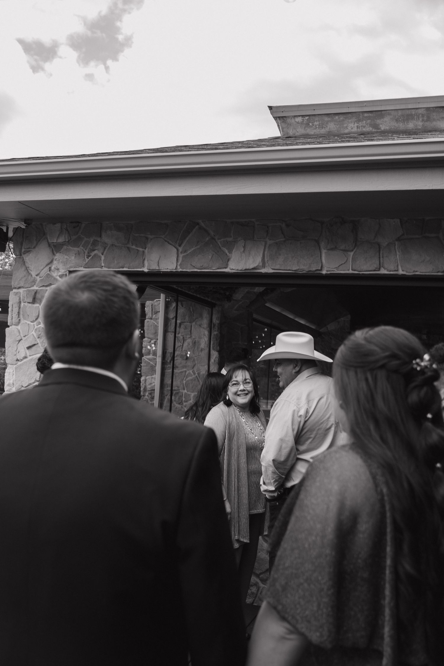 Wedding guests greet each other outside a stone building entrance in this classic black and white photo.