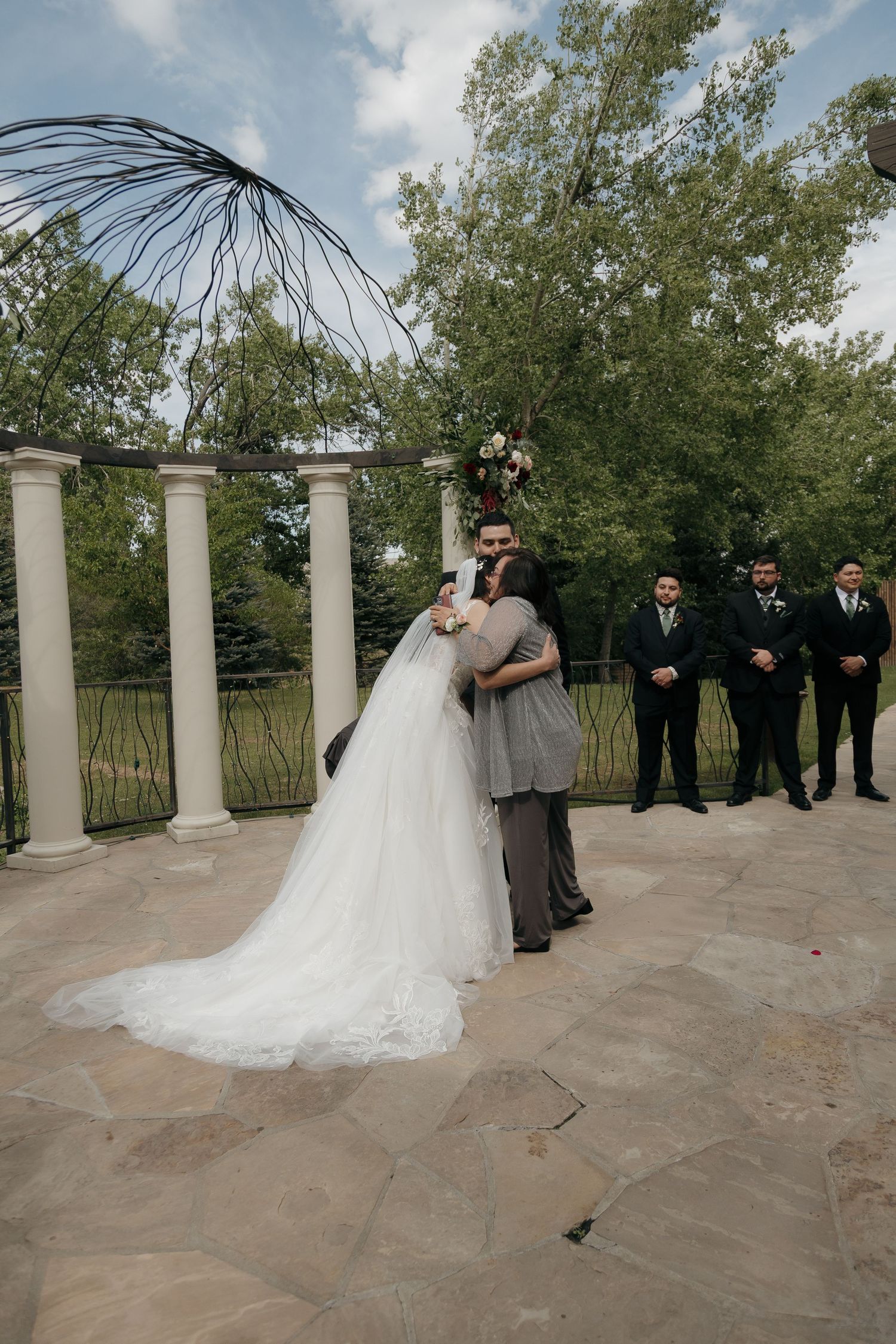 Bride in white gown and groom share first kiss at outdoor wedding ceremony with white columns.