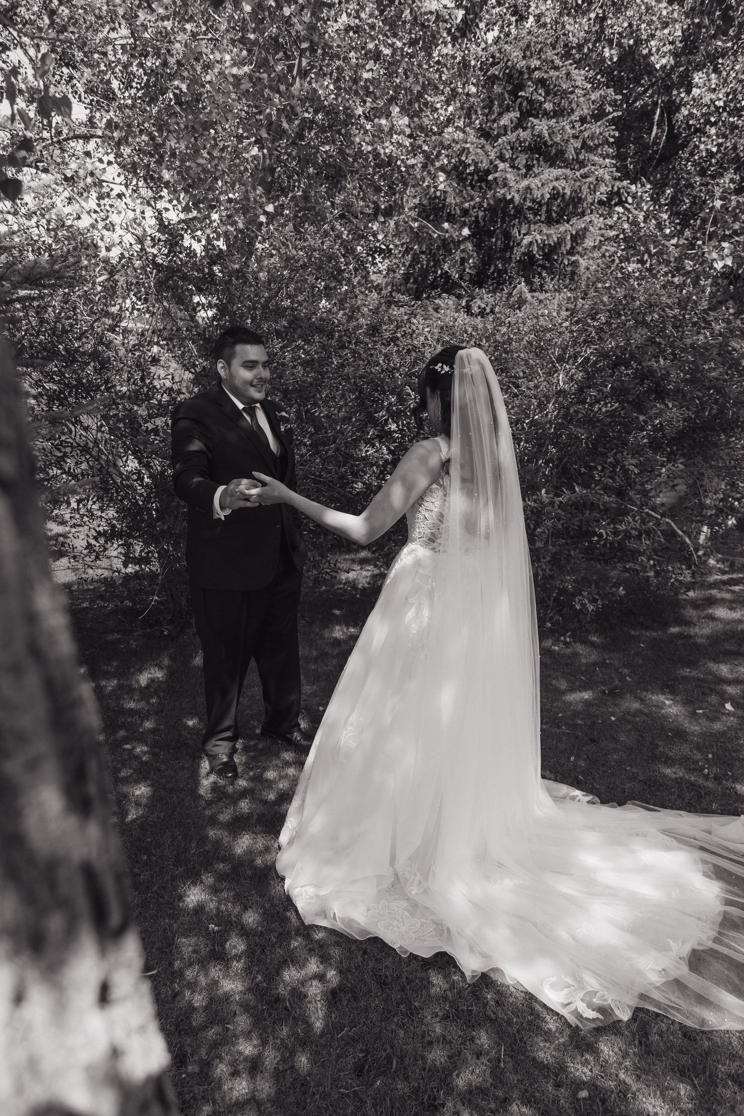 Black and white photo of bride and groom holding hands in lush garden setting.