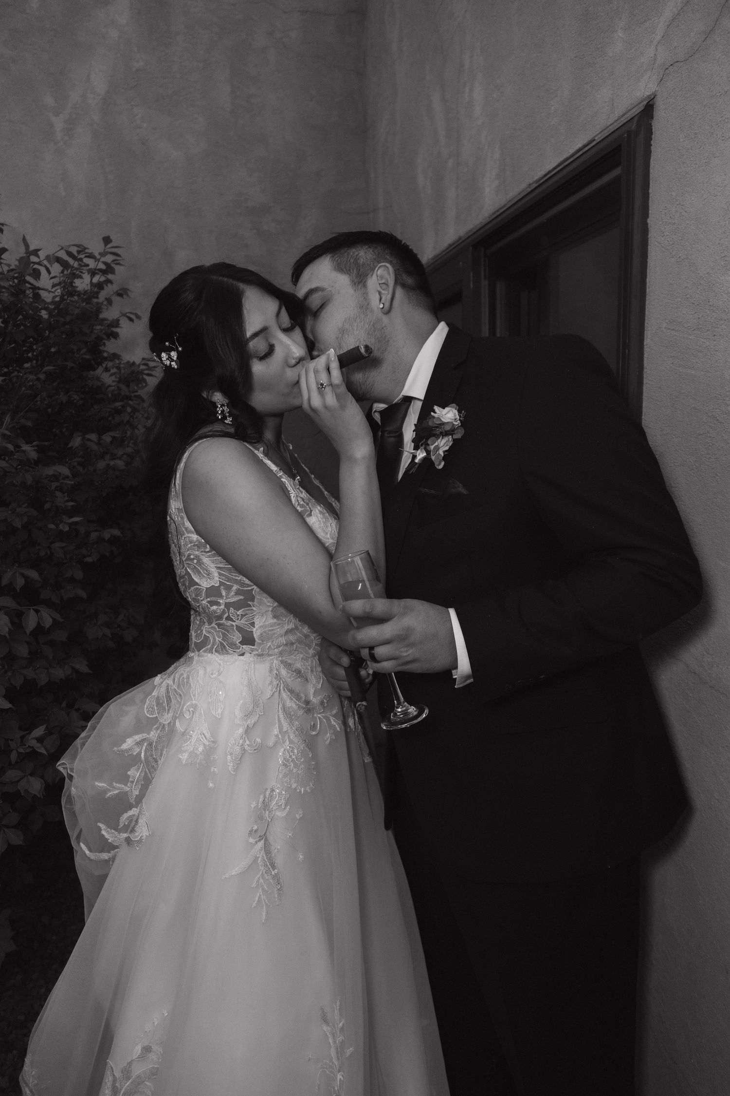 Black and white photo of bride and groom sharing an intimate kiss while holding a champagne glass.