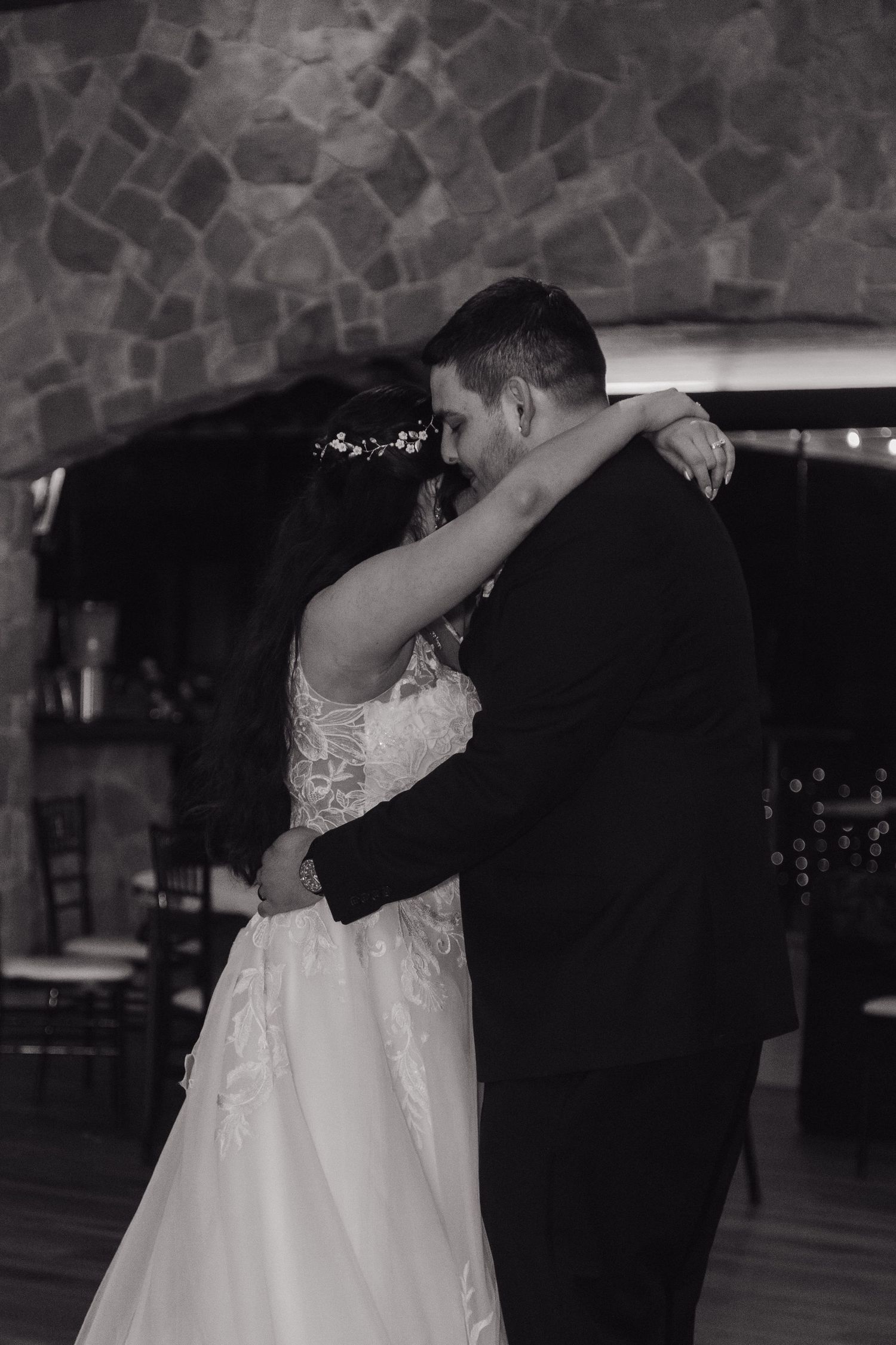 Black and white romantic first dance photo of bride and groom embracing in stone venue.