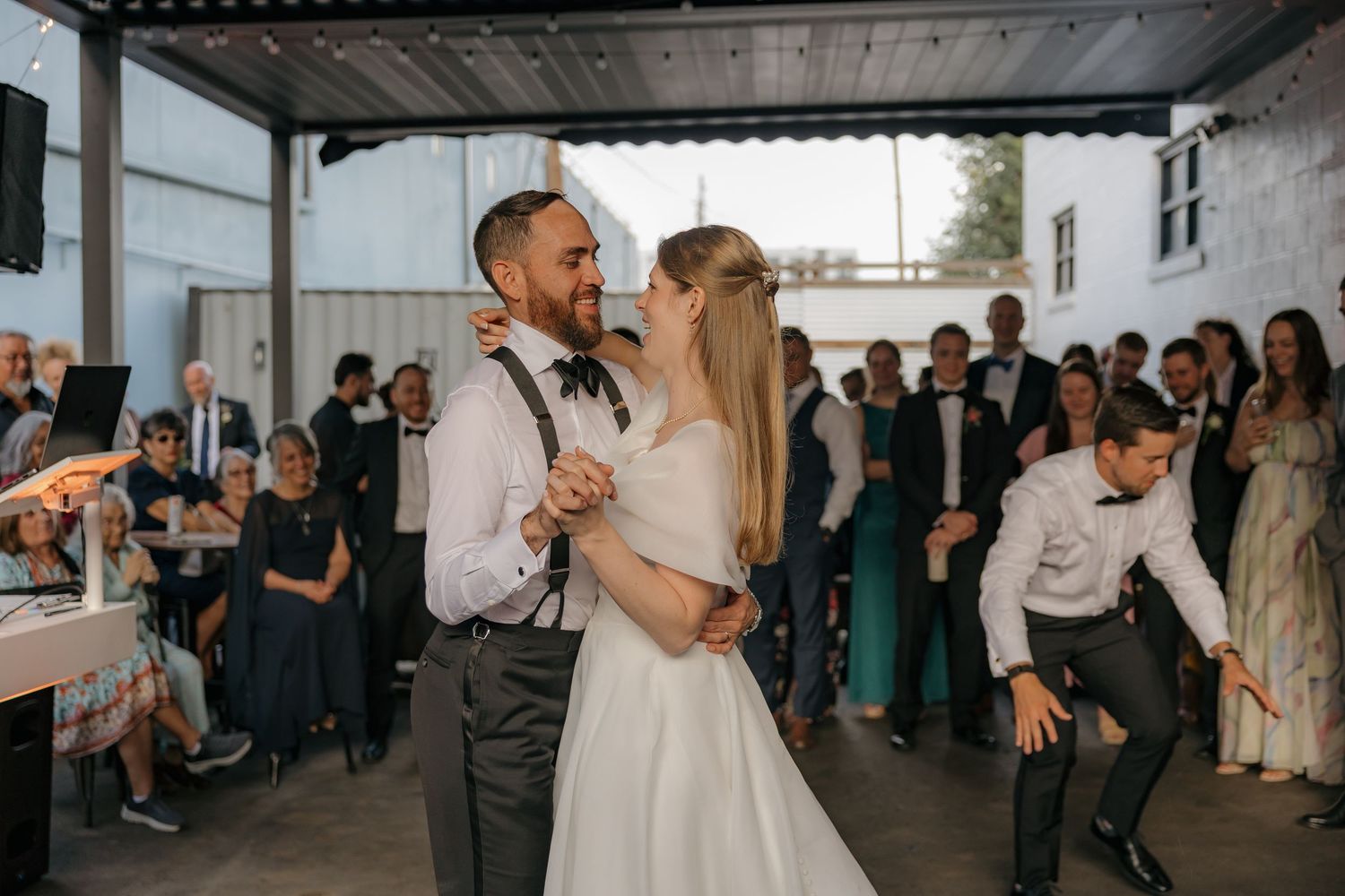 Bride and groom sharing first dance surrounded by wedding guests at outdoor reception venue.
