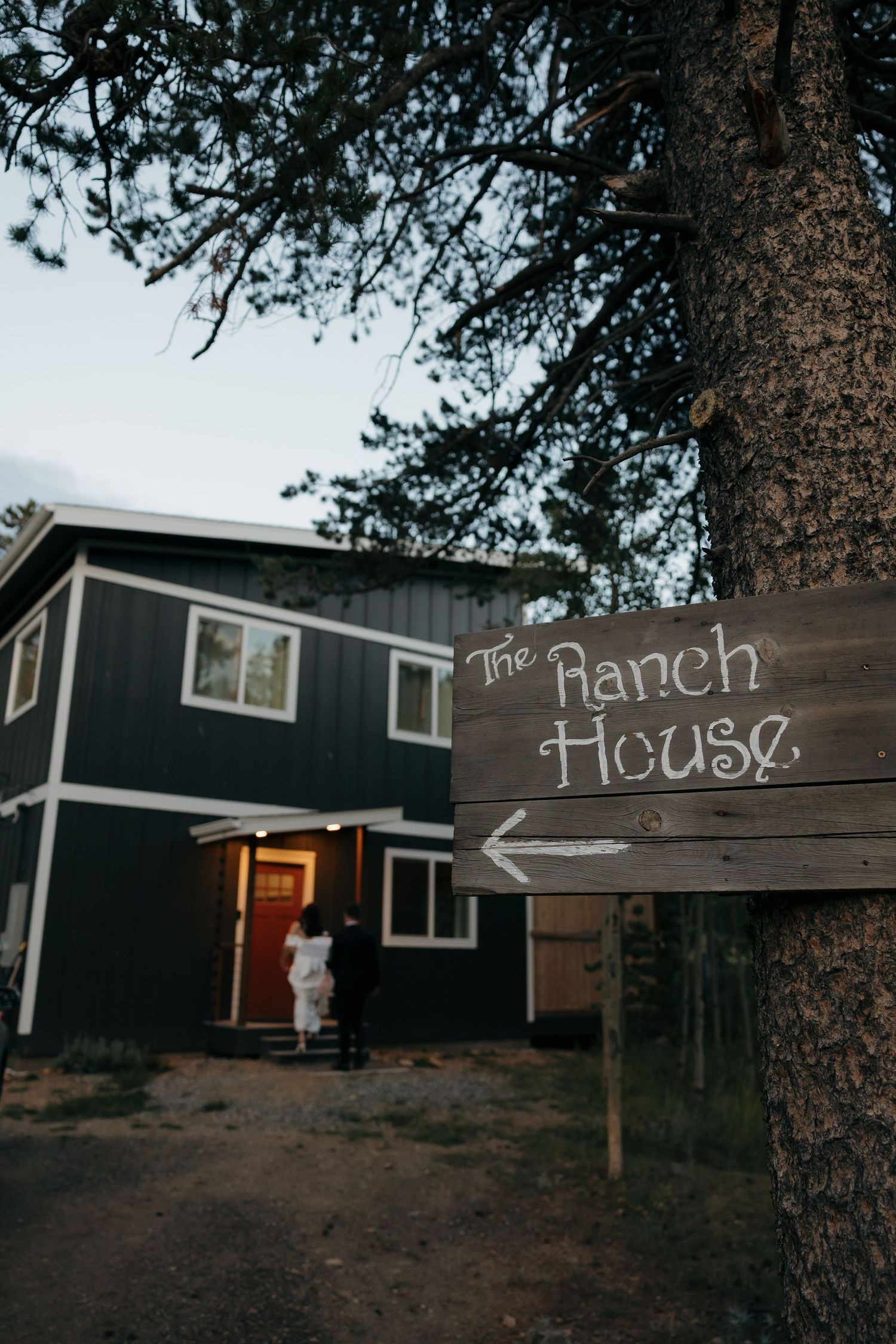 Rustic wooden Ranch House sign on a pine tree outside a dark blue two-story building at dusk.