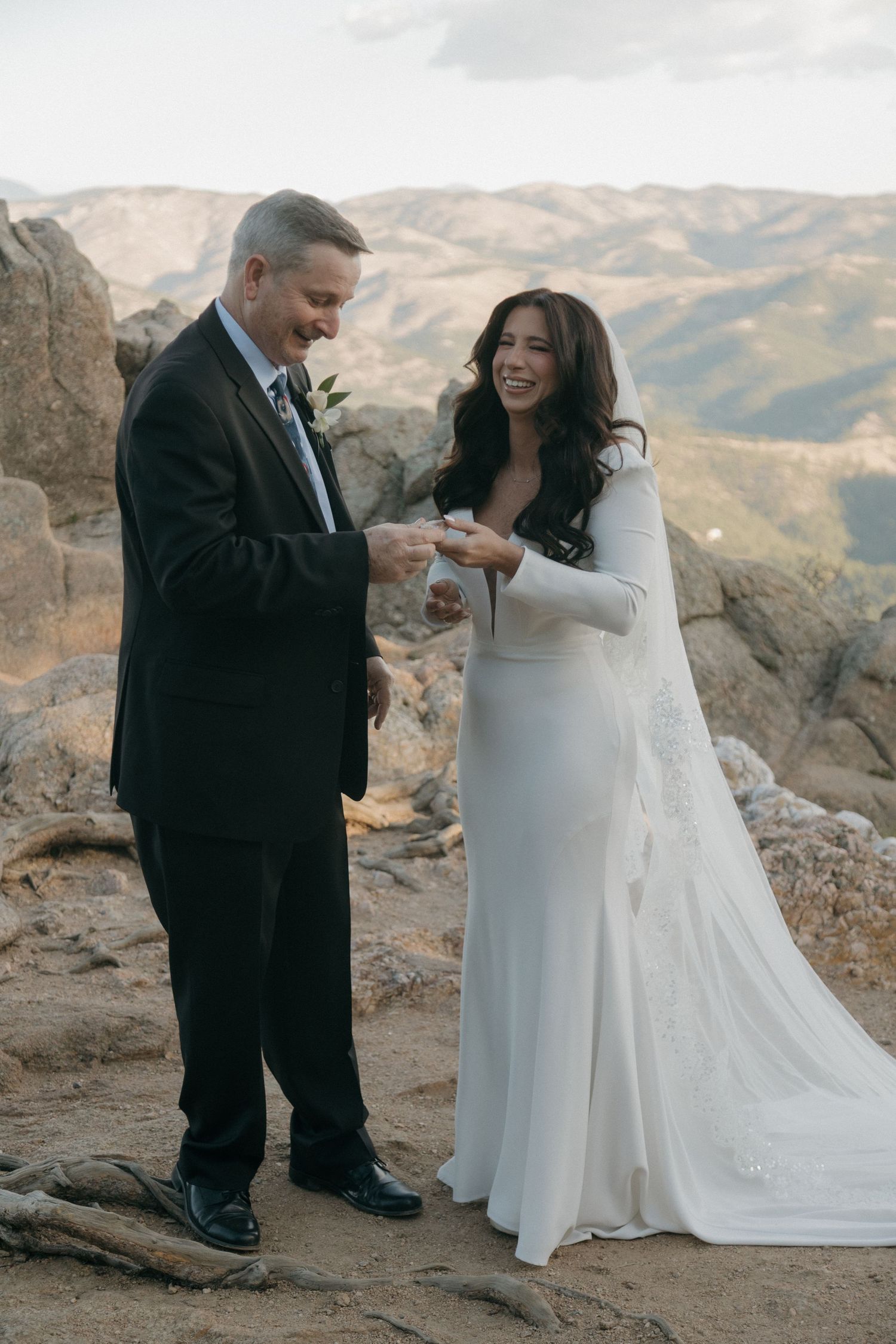 Couple laughing during ring exchange ceremony on a stunning rocky mountain summit.