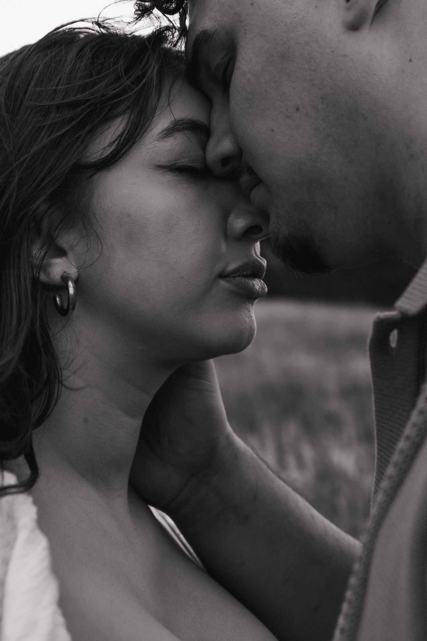 Intimate black and white close-up of couple nearly kissing, eyes closed, outdoors.